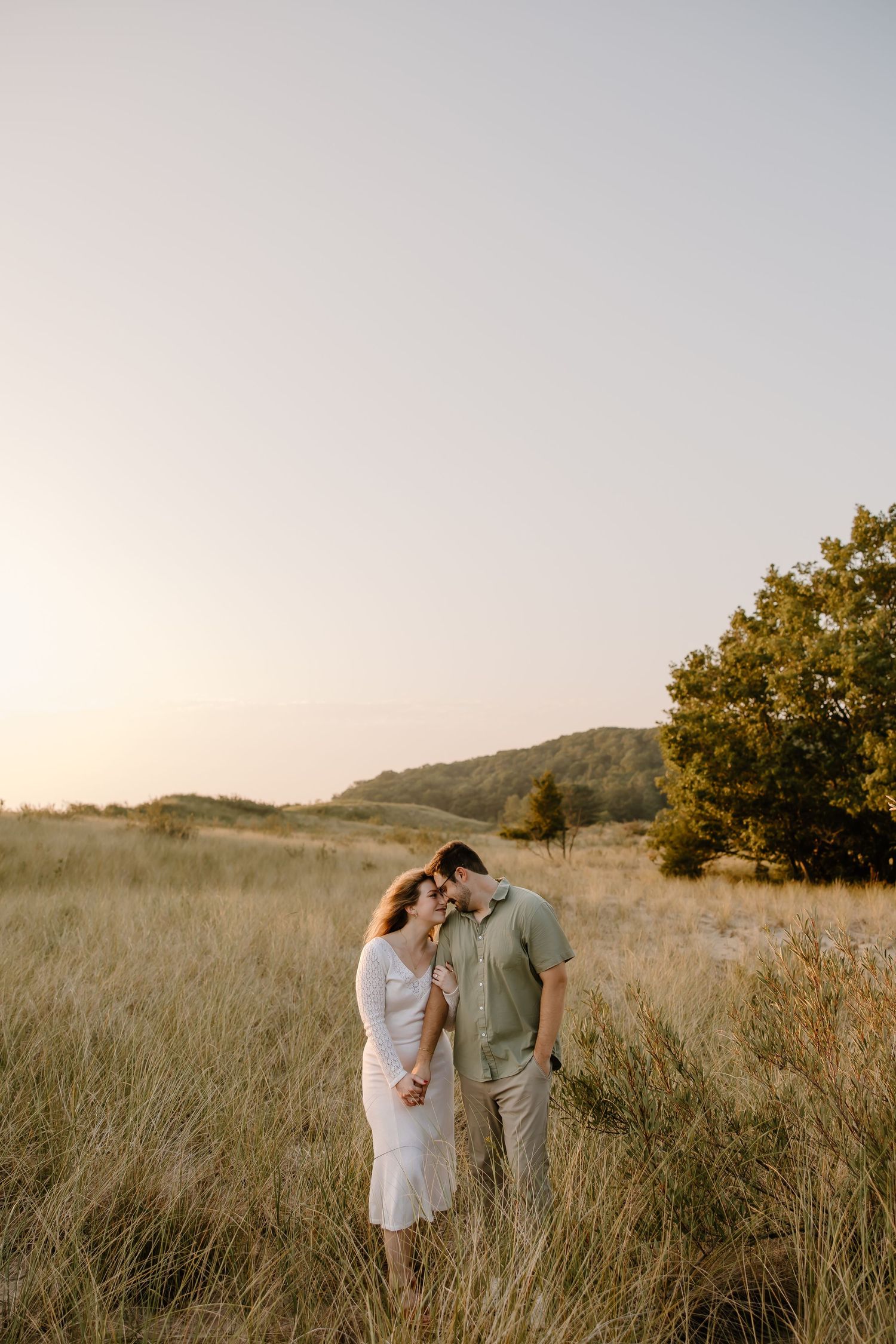 A couple poses together in a golden field with soft lighting and natural scenery.