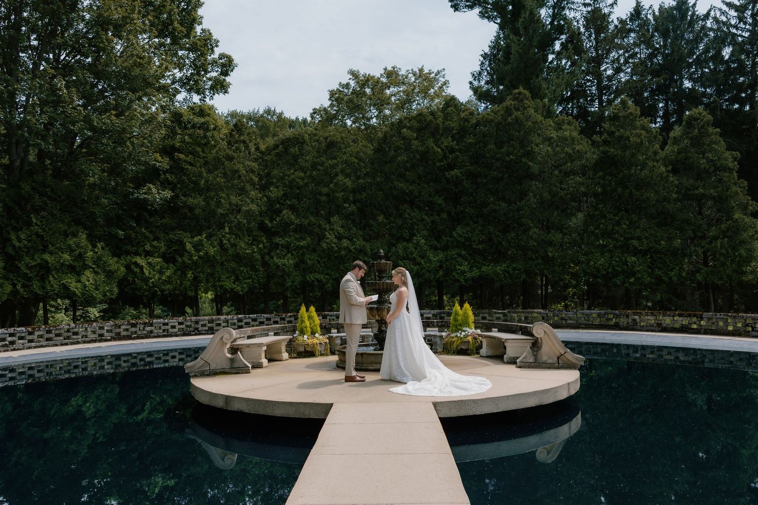 Bride and groom exchange vows on a circular platform over a serene pool surrounded by lush greenery.