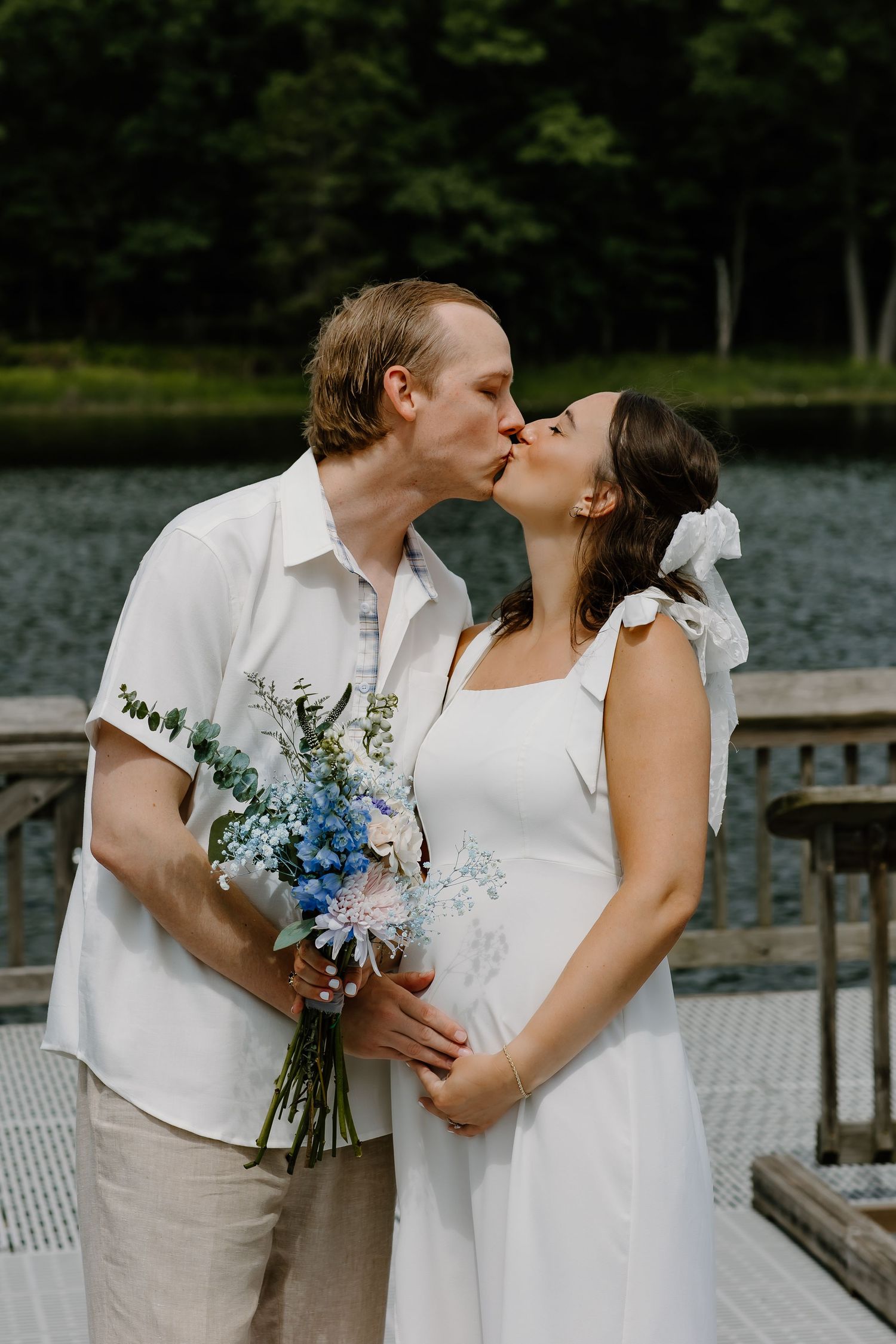 A romantic wedding moment captured on a dock with a beautiful blue and white floral bouquet.