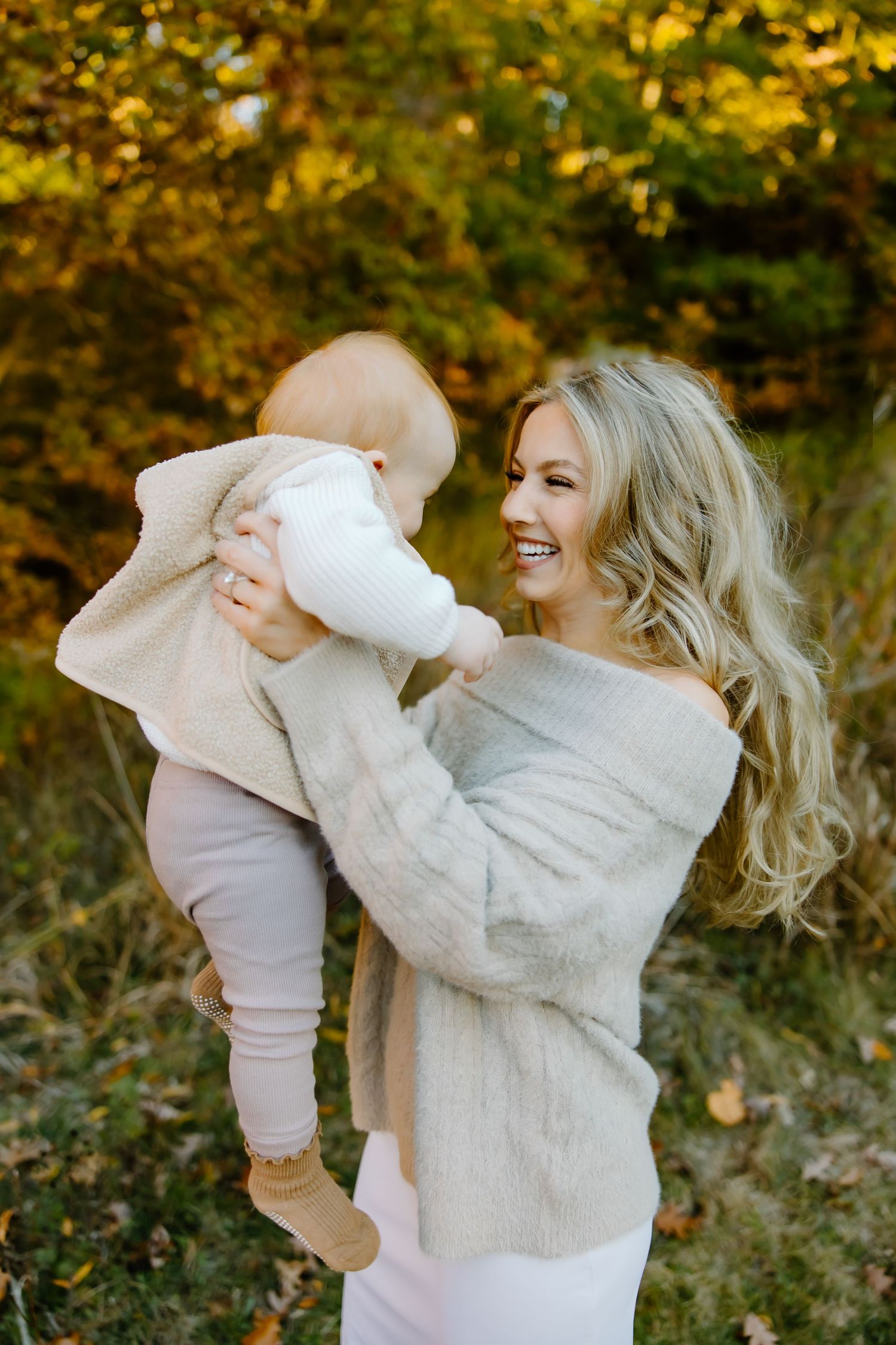 Parent and baby sharing joyful moment outdoors in autumn setting.