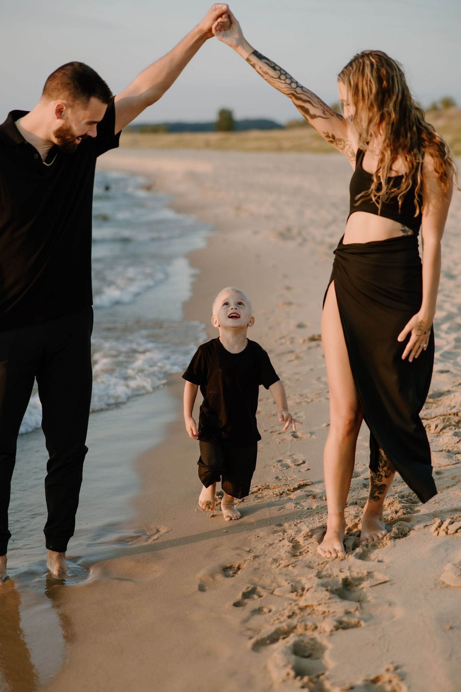 Family playing and dancing together on beach at sunset.