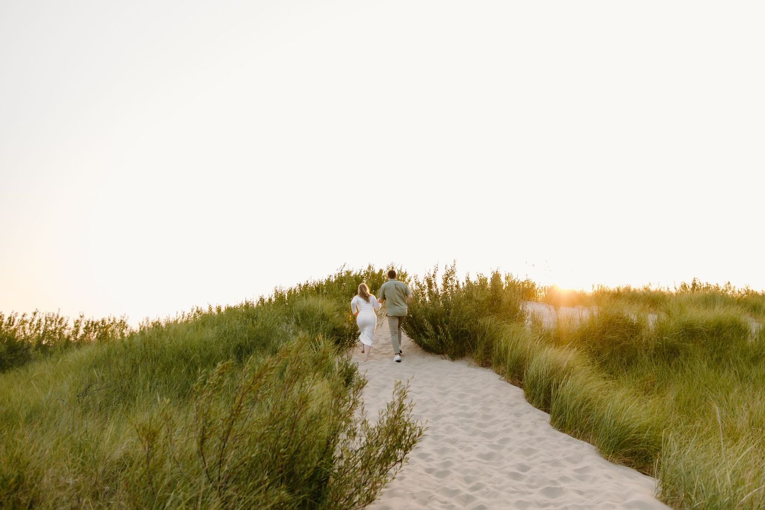 A sandy beach path leads through dunes during a romantic sunset photoshoot.