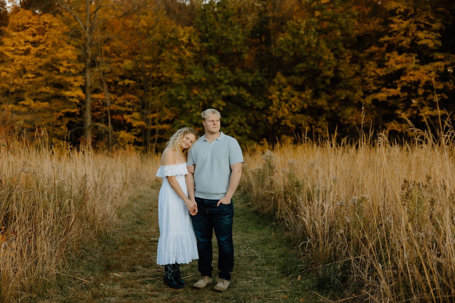 Wide landscape view of couple walking through autumn field with golden trees.