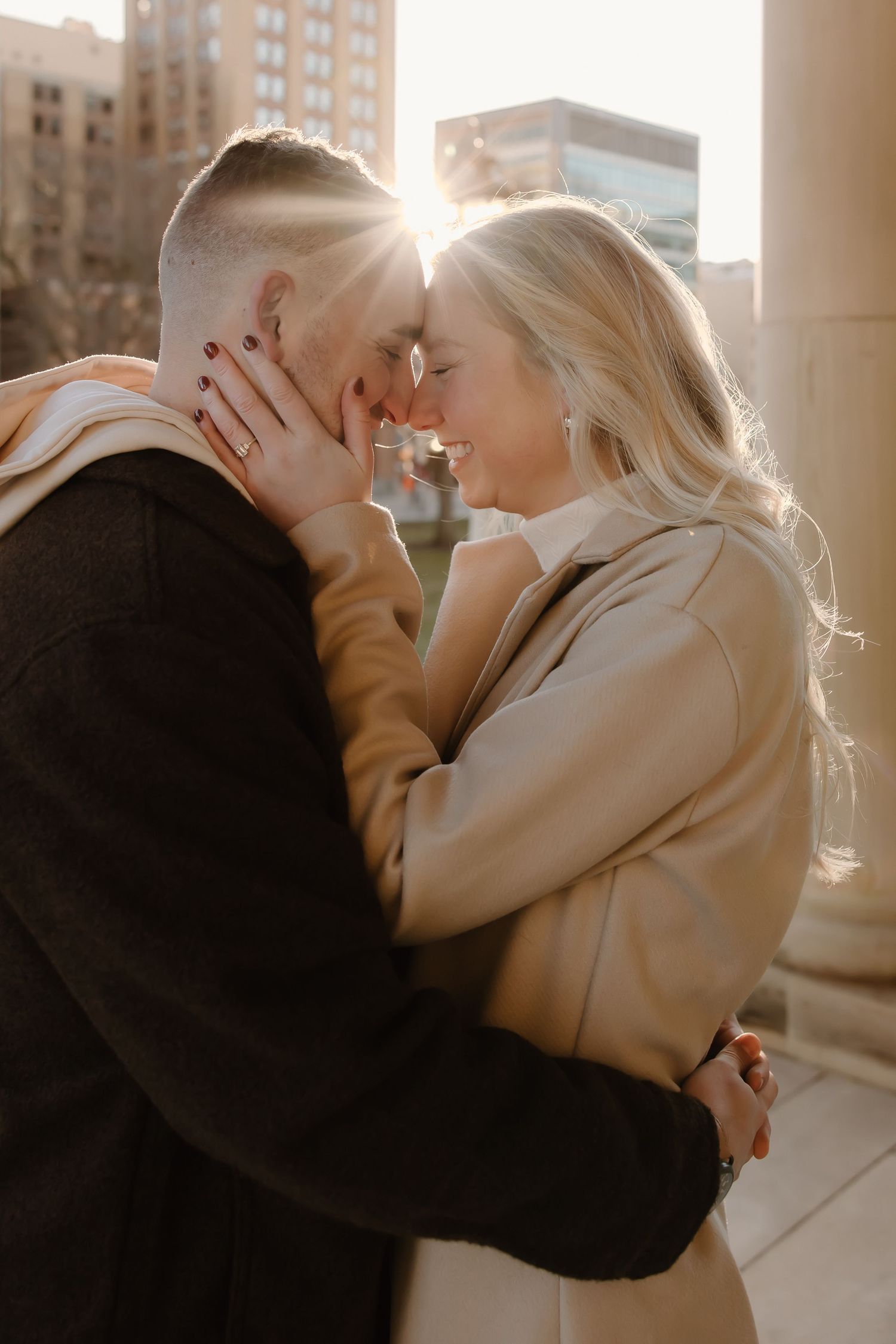 A tender moment between two people in warm sunlight against an urban backdrop.
