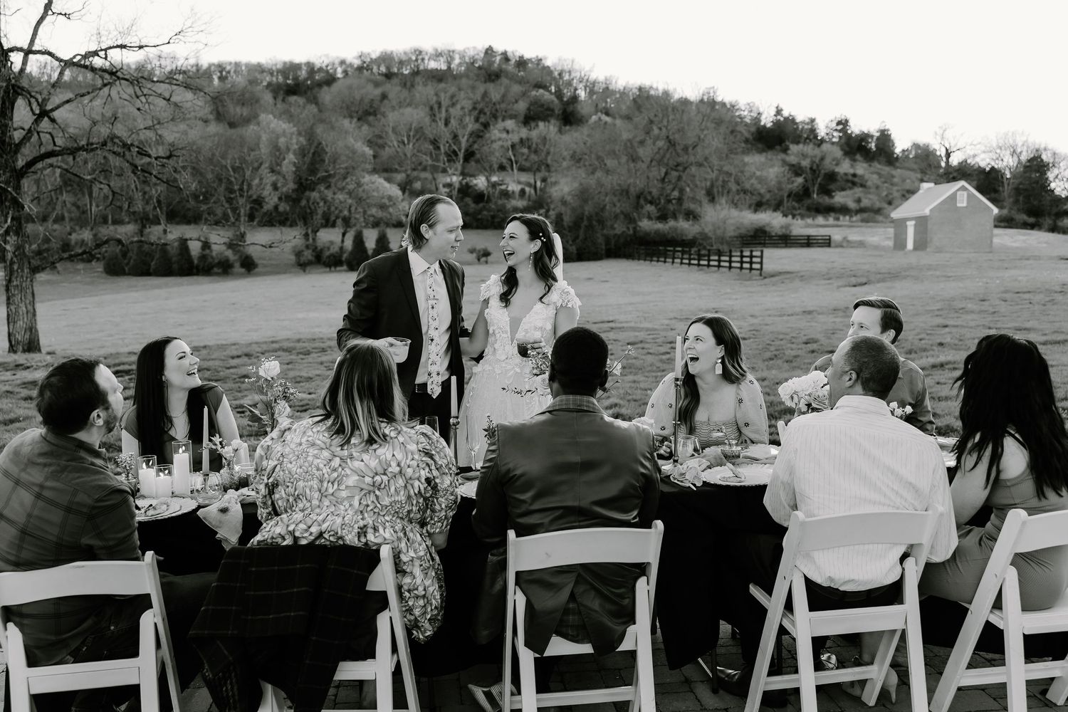 Panoramic view of wedding guests seated in white chairs at an outdoor ceremony.