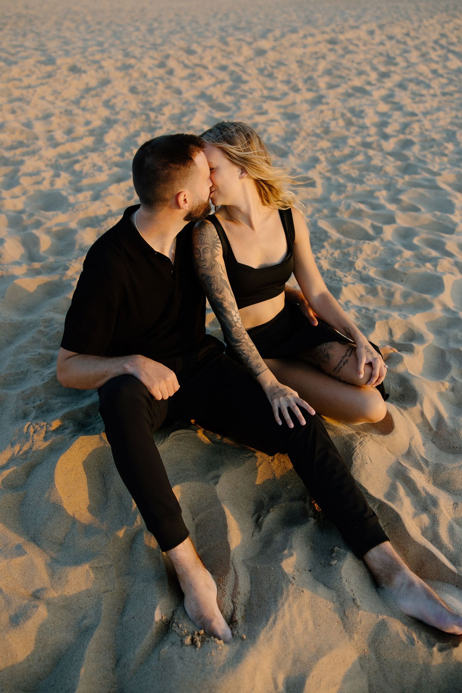Intimate moment shared between couple sitting on sun-warmed beach sand.