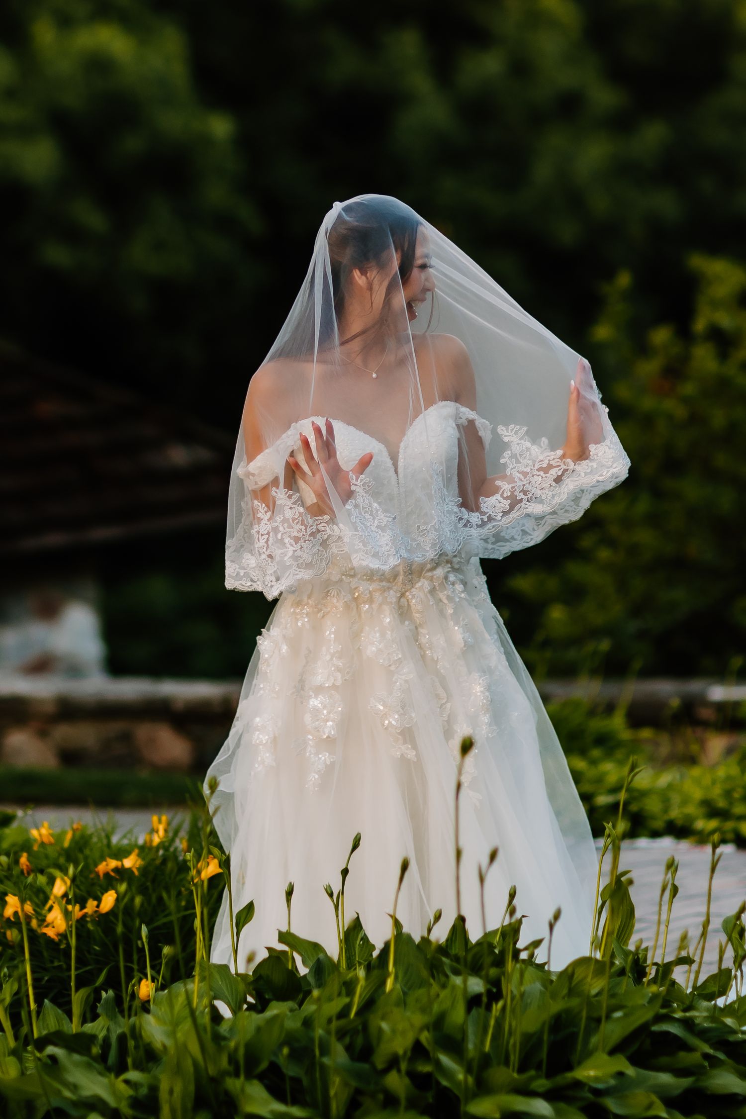 White wedding dress with lace details photographed in a garden with yellow flowers.