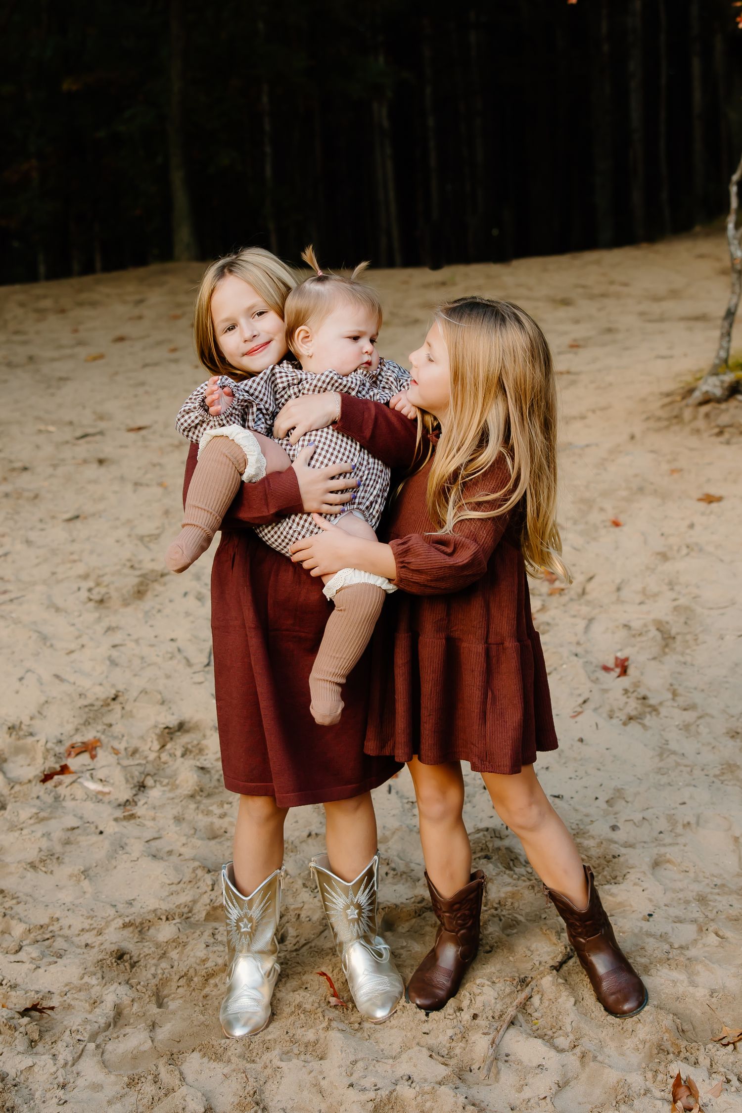 Children in matching burgundy outfits play together on sandy ground during fall photo session.