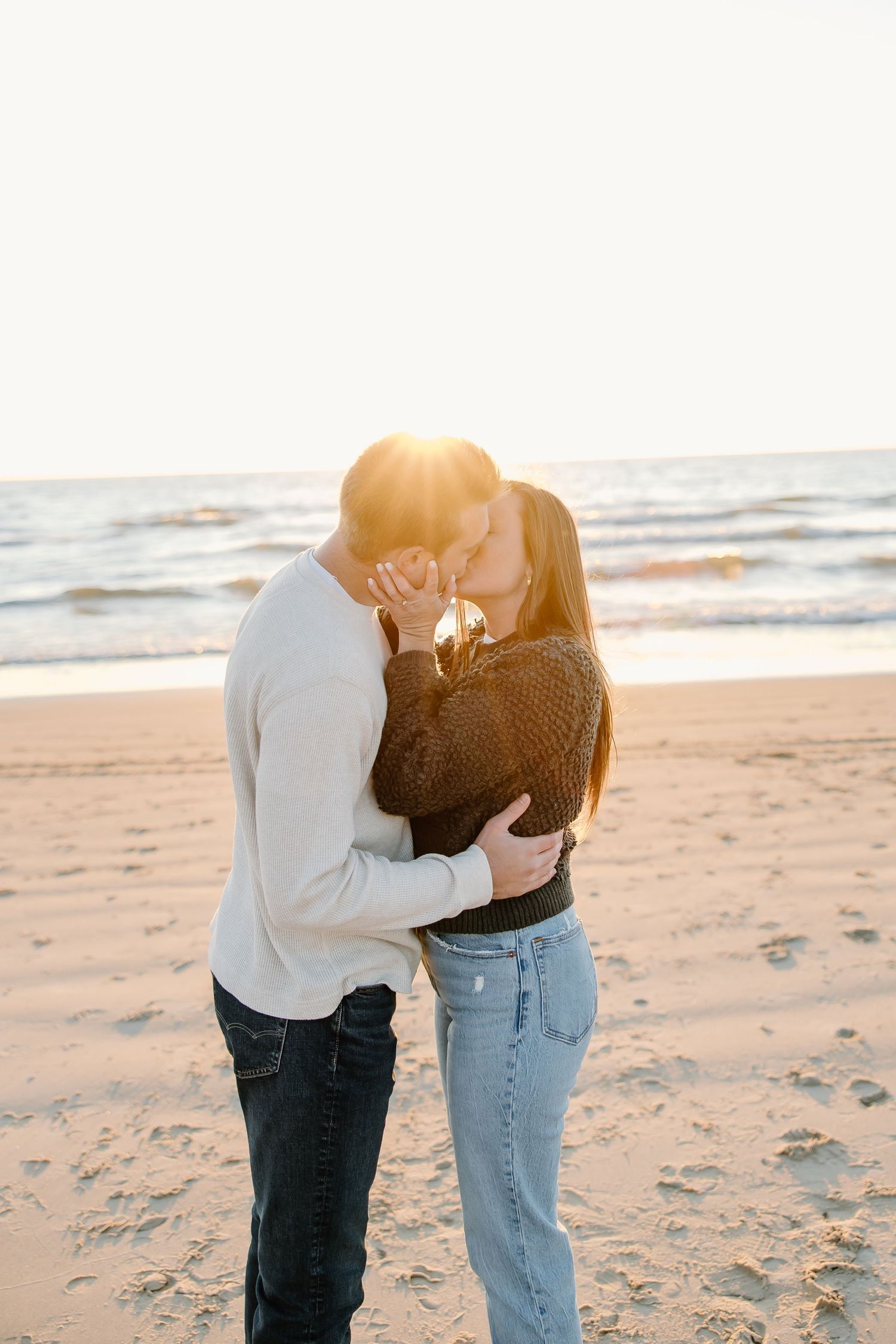 A couple sharing a tender moment on a sunlit beach at golden hour.