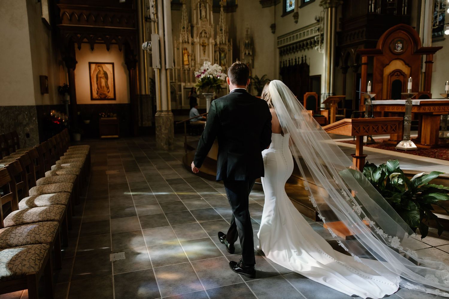 Long cathedral aisle with dramatic lighting and flowing white wedding dress train.