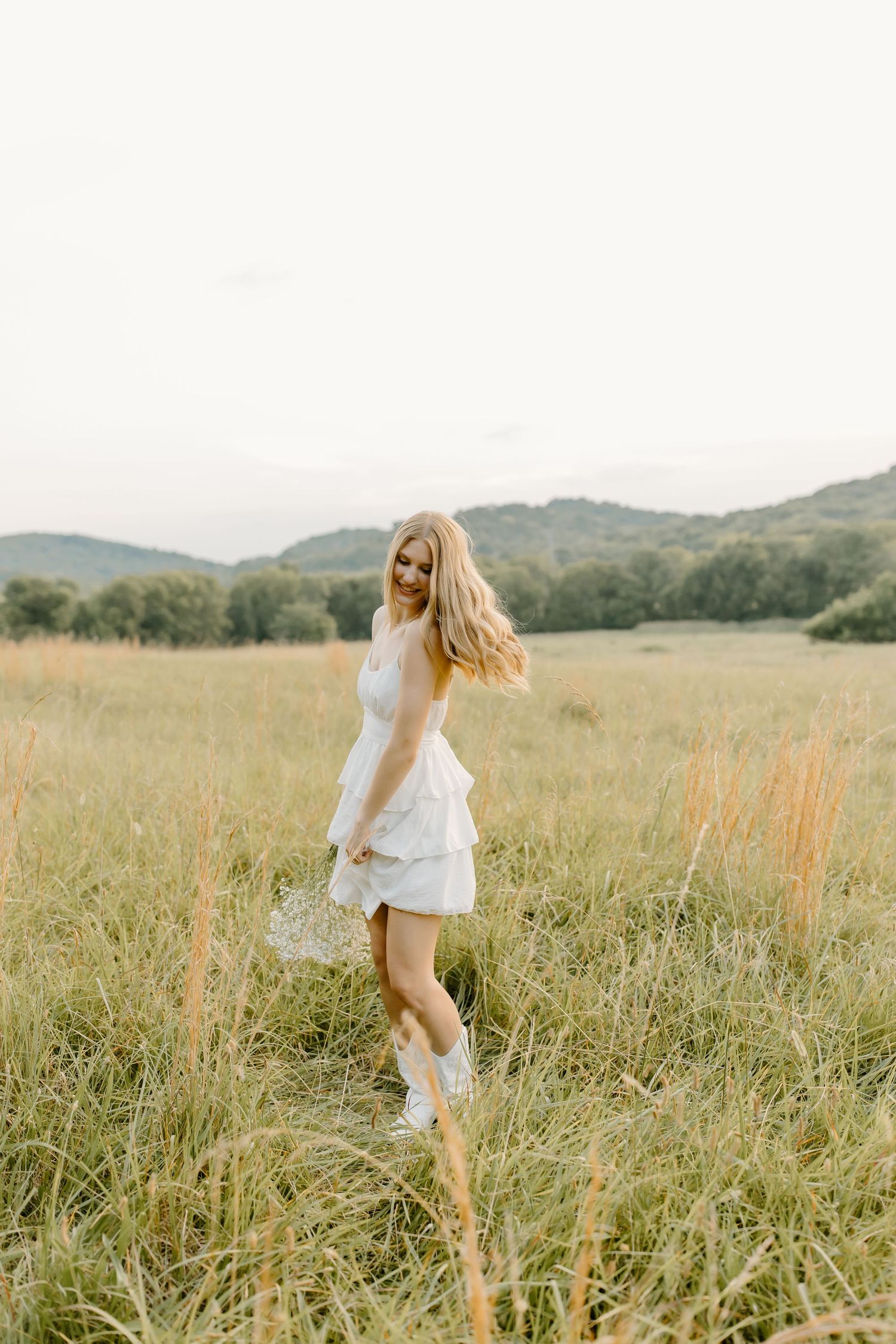 A person in a white dress spins joyfully in a golden meadow with rolling hills in the background.