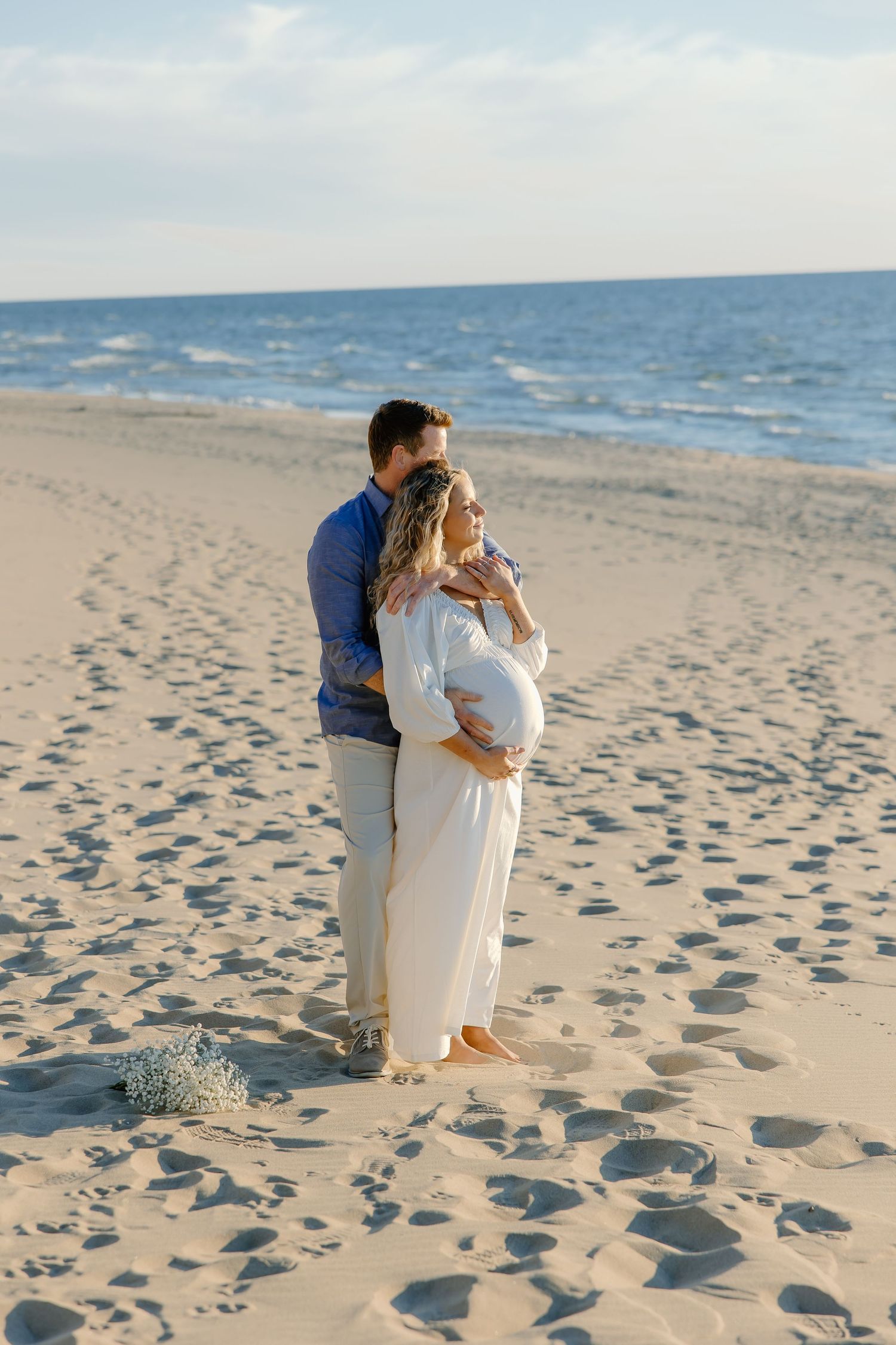 Couple embraces on sandy beach with ocean waves in background during sunset.