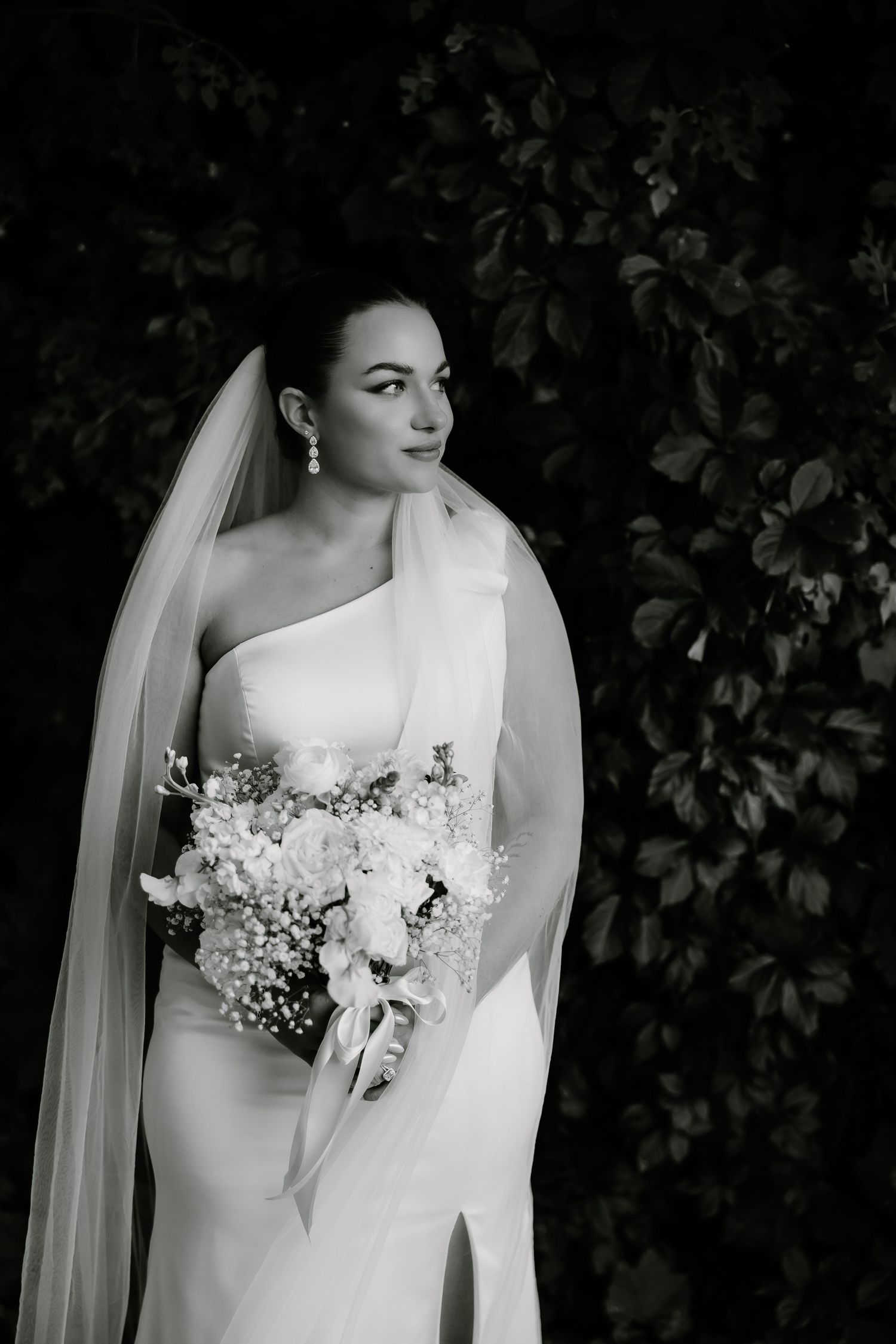 Black and white portrait series of a bride in an elegant white gown with long veil holding a delicate floral bouquet.