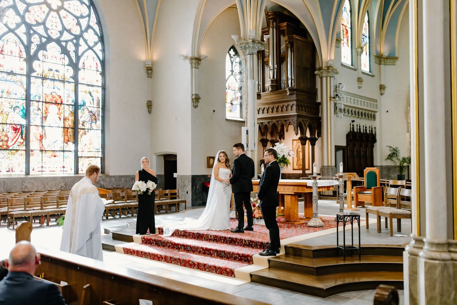 Elegant church interior with stained glass windows and white columns illuminated during a wedding service.