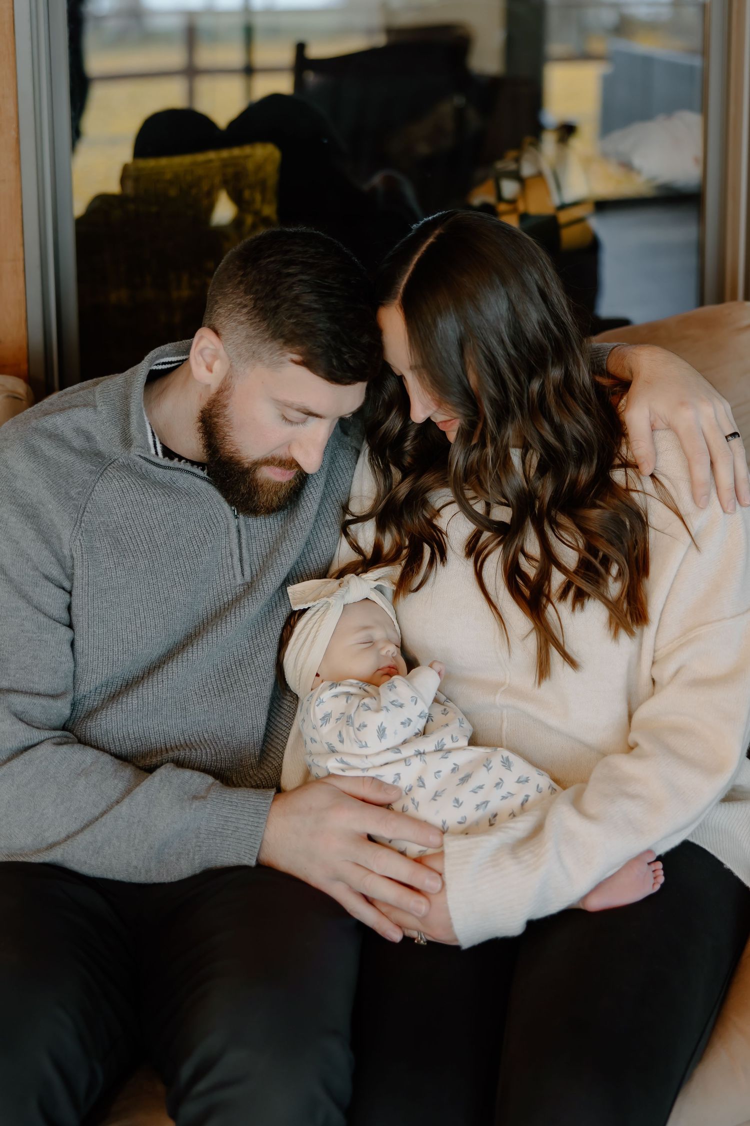 A couple sits together on a couch while holding their newborn baby in a tender family moment.