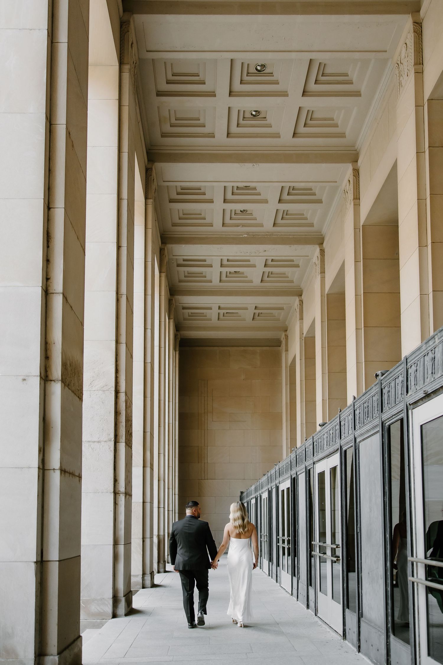 Couple walks through elegant columned hallway with coffered ceiling.