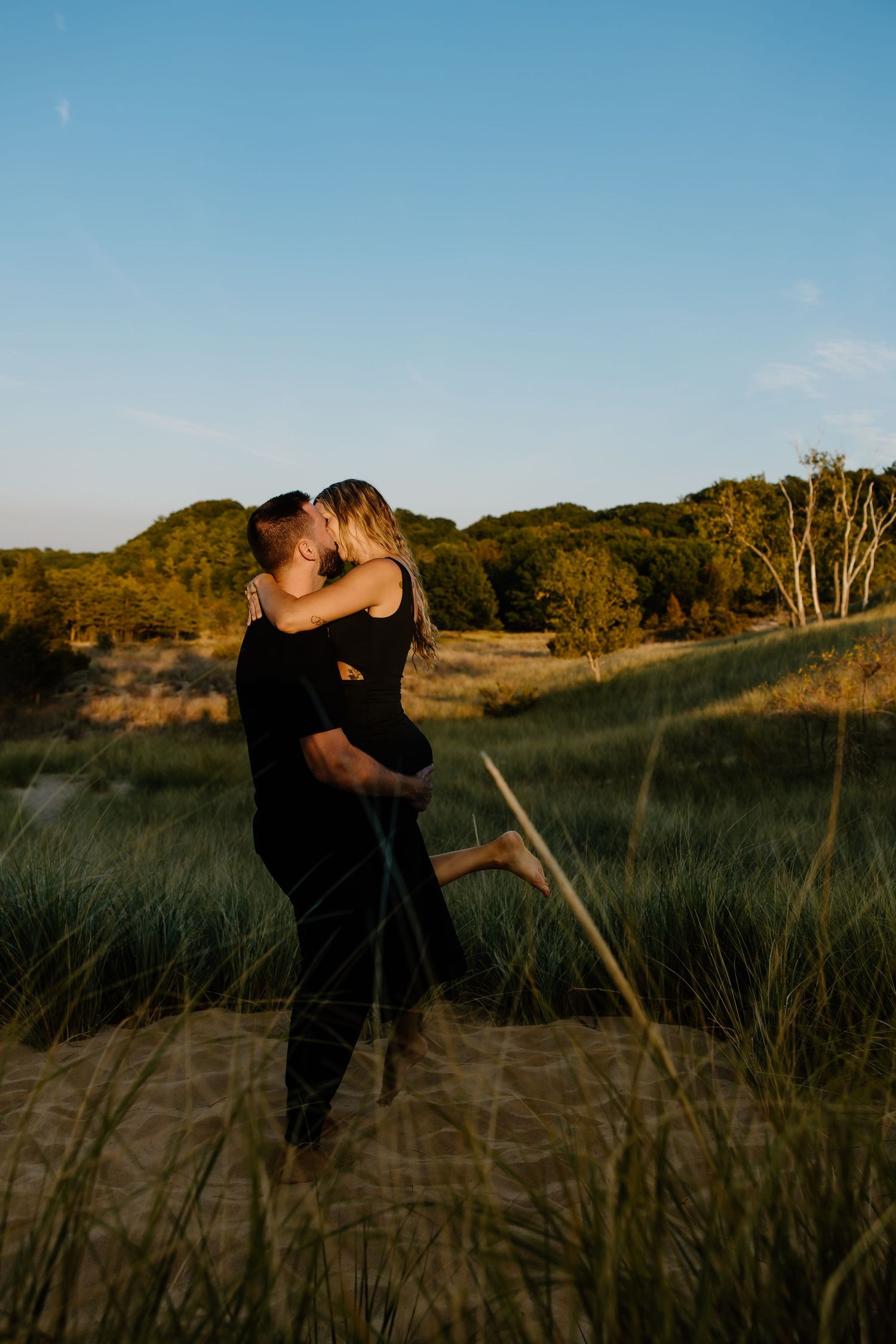 Romantic sunset embrace in a grassy coastal landscape.