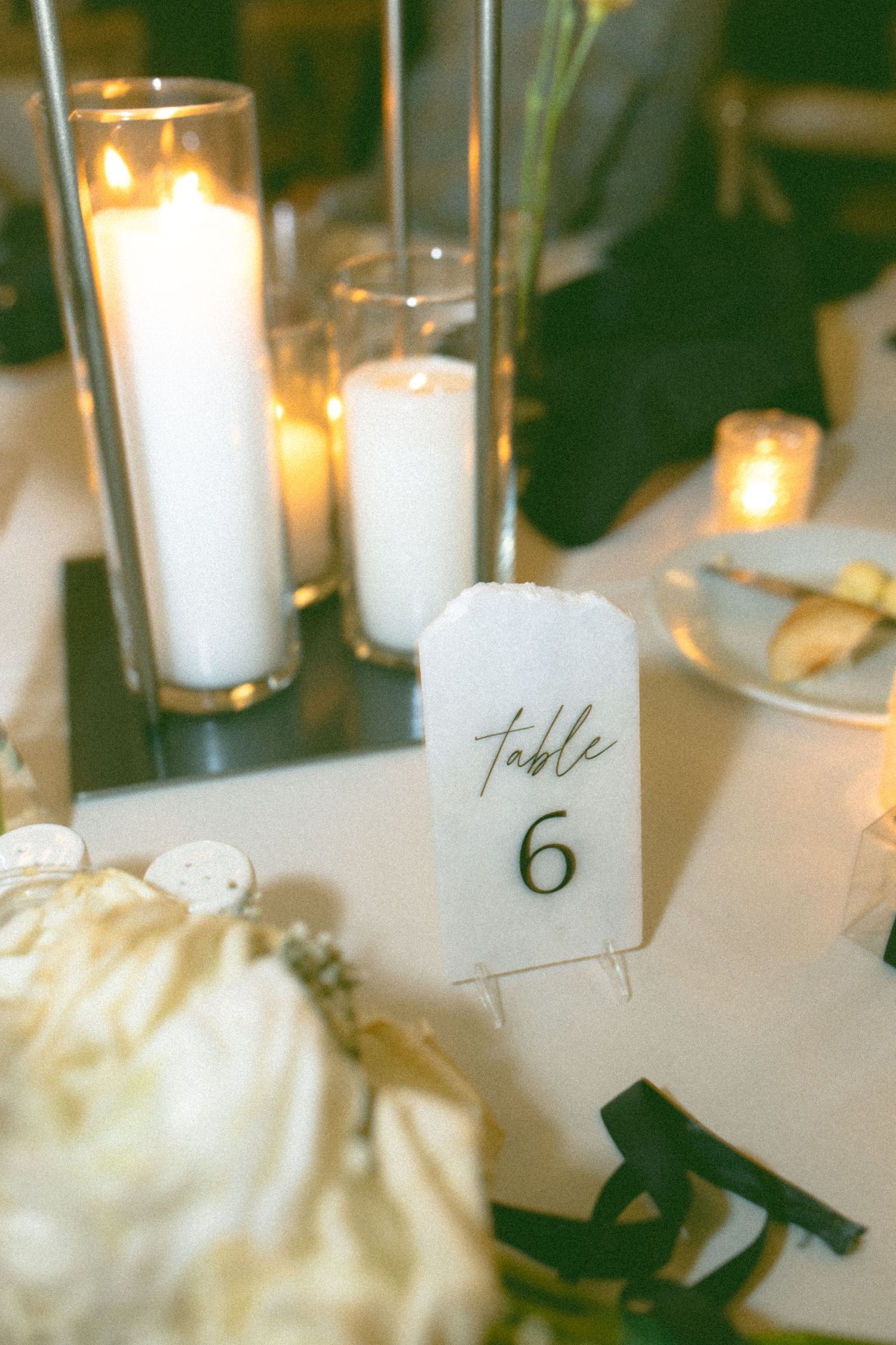 Wedding table decor with white candles, table numbers and elegant place settings.