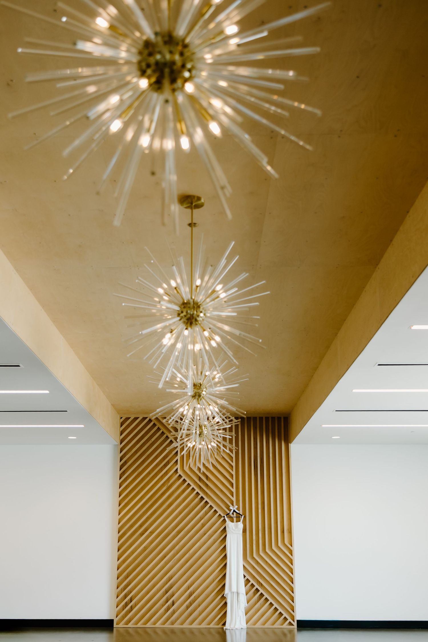 Modern starburst chandelier with gold accents mounted on a white ceiling with geometric wood wall details.
