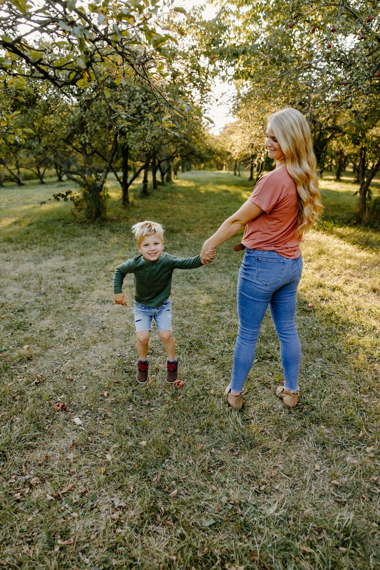 Two people holding hands while walking through an orchard at golden hour.