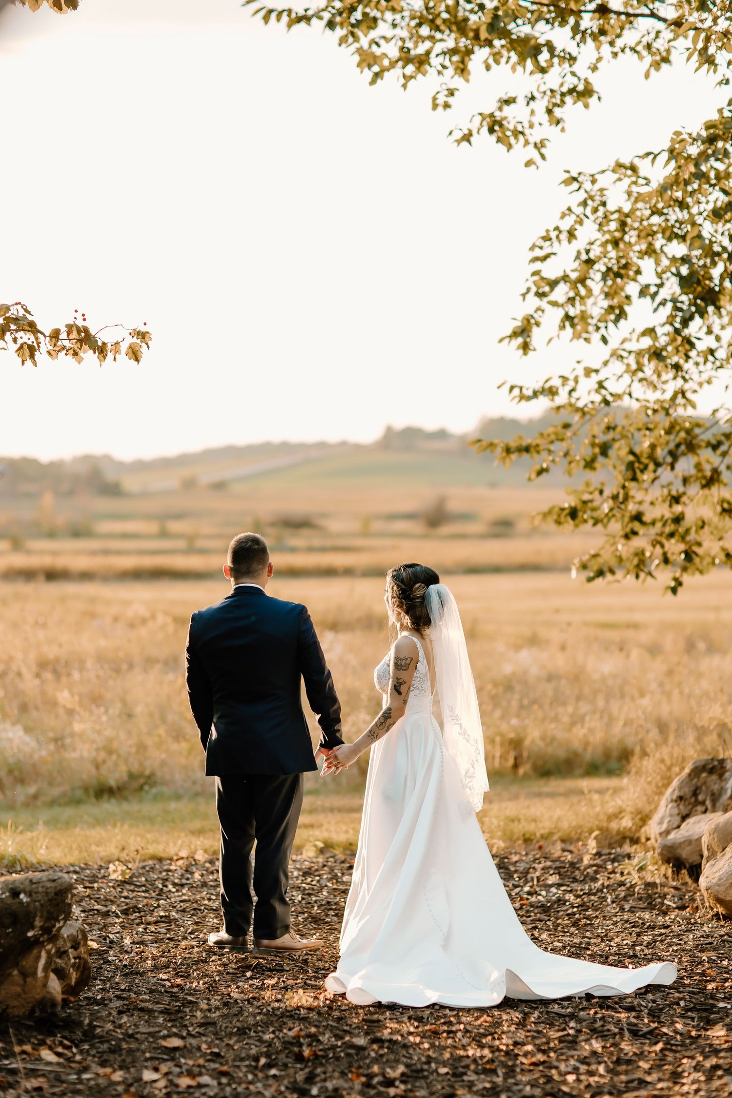 Scenic wedding portraits of couple walking through autumn field at golden hour.