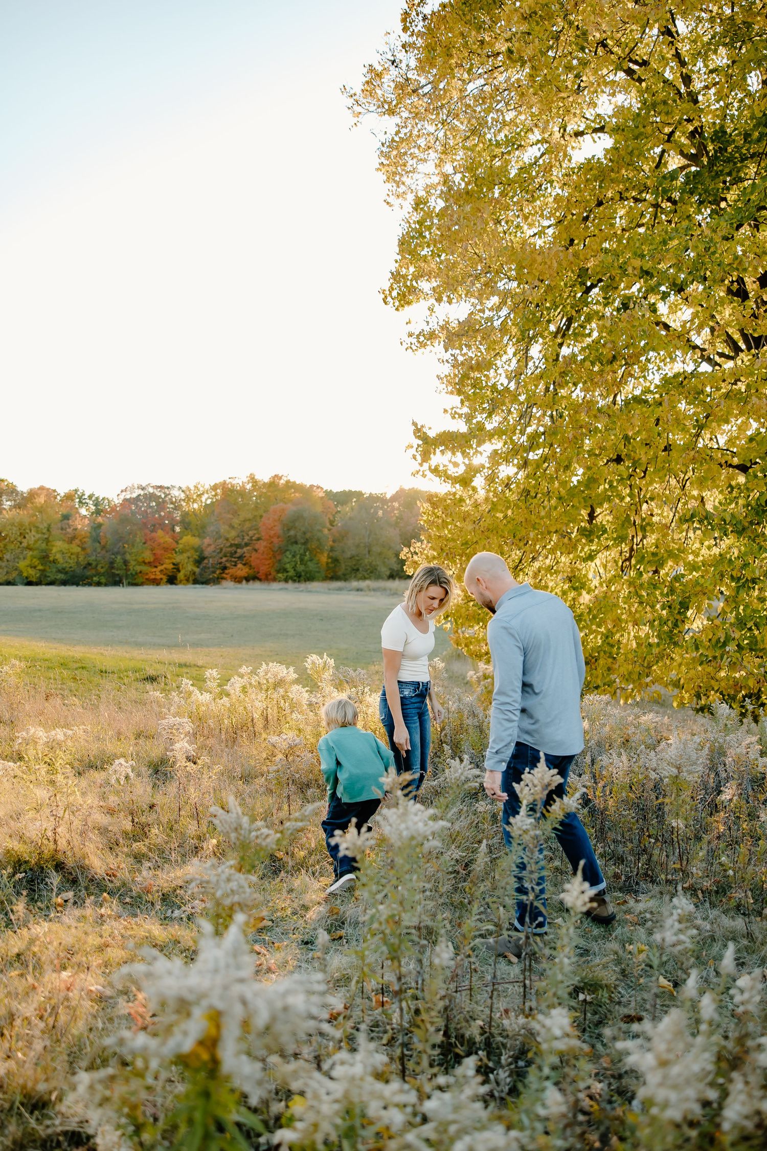 Family enjoying a playful moment together in a sunlit meadow with fall foliage.
