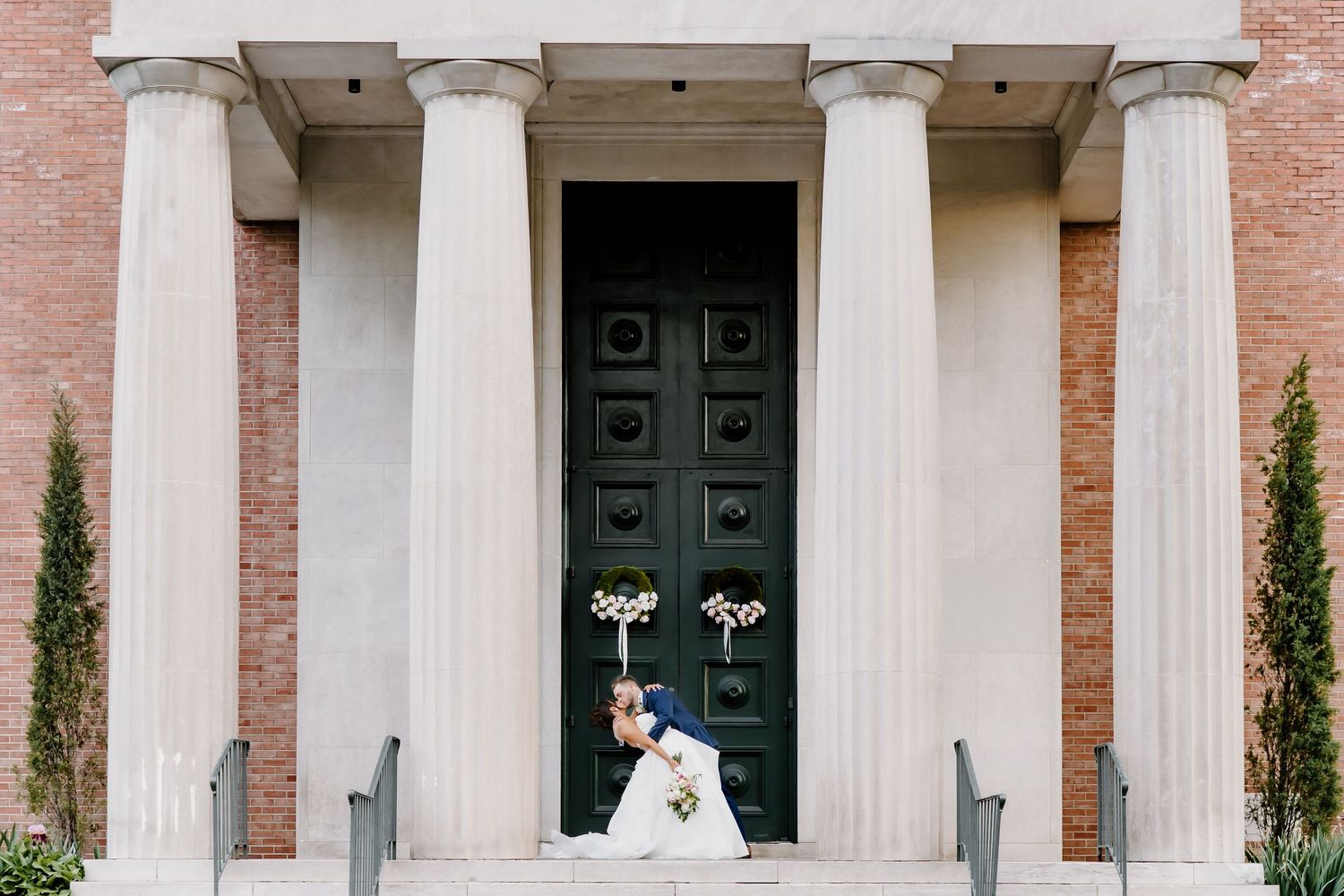 Elegant brick building facade with white columns and dark doors.