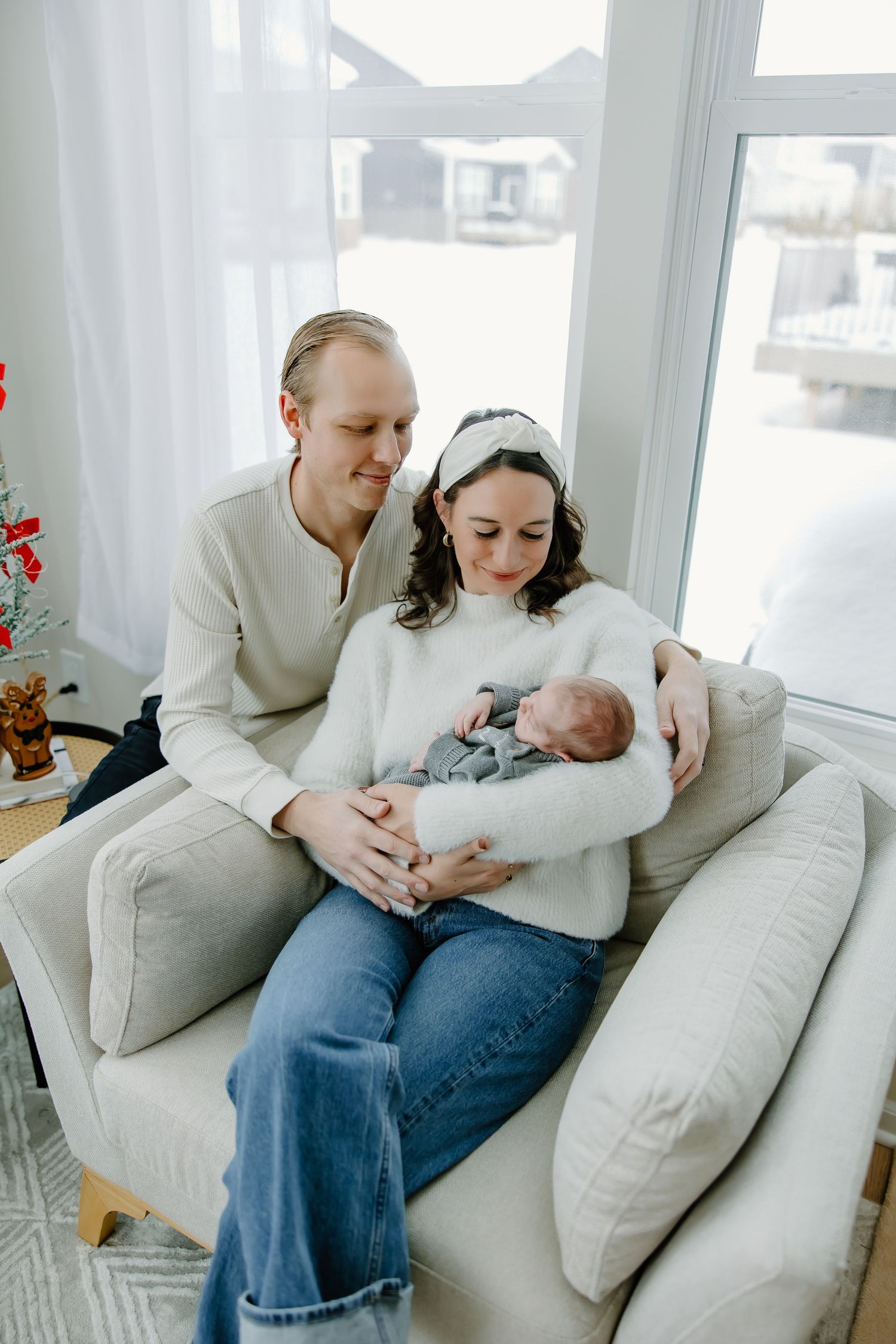 Candid moments of a family relaxing together on a light gray couch by large windows.