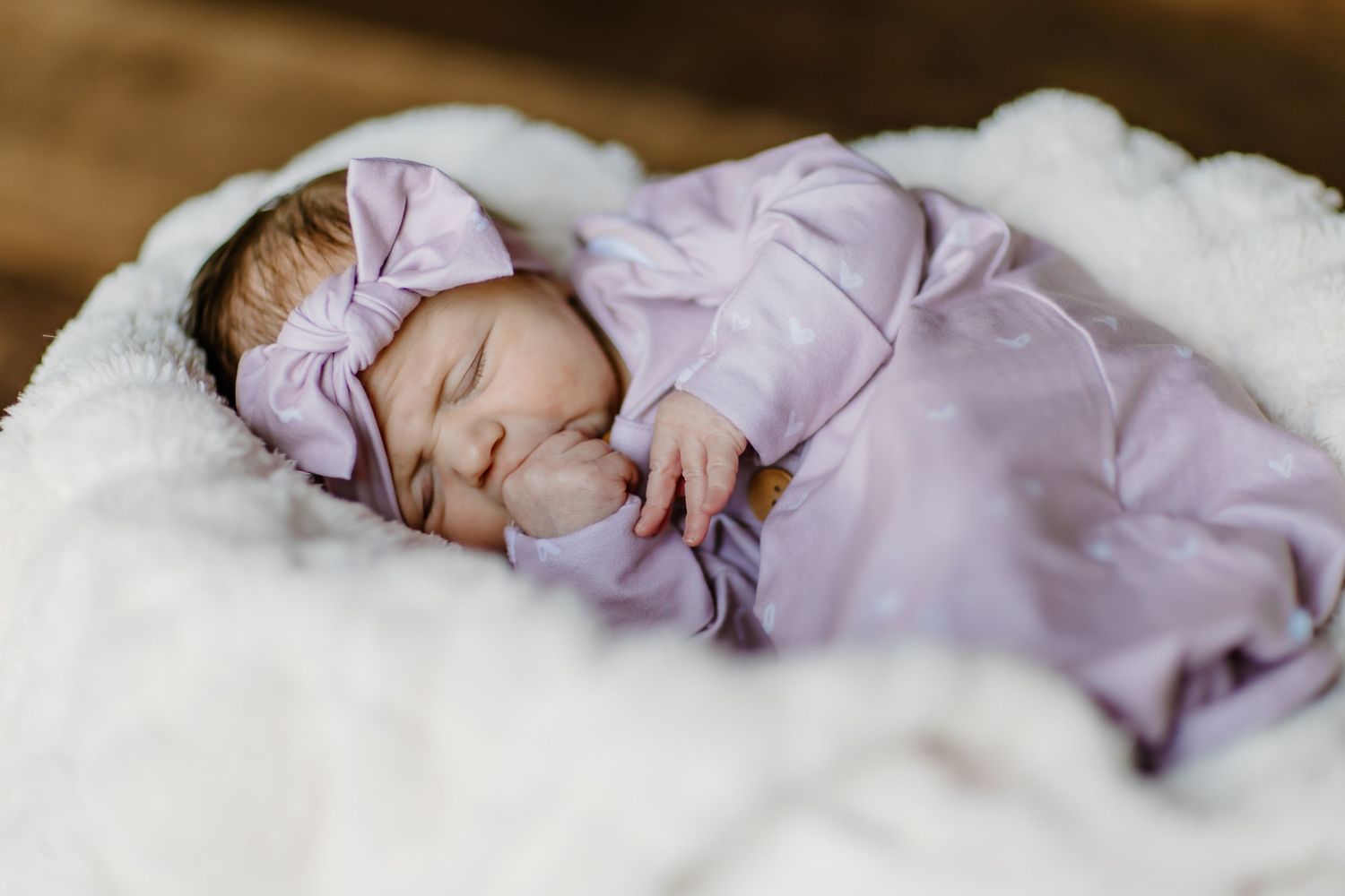 Baby in lavender outfit sleeping peacefully on white bedding.