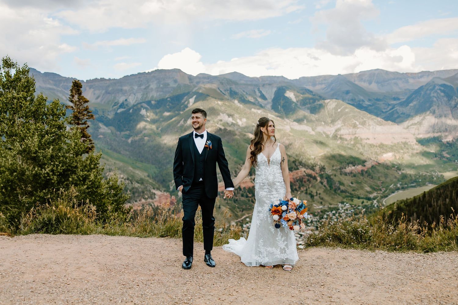Wedding couple poses together on a scenic mountain overlook with dramatic mountain ranges in the distance.