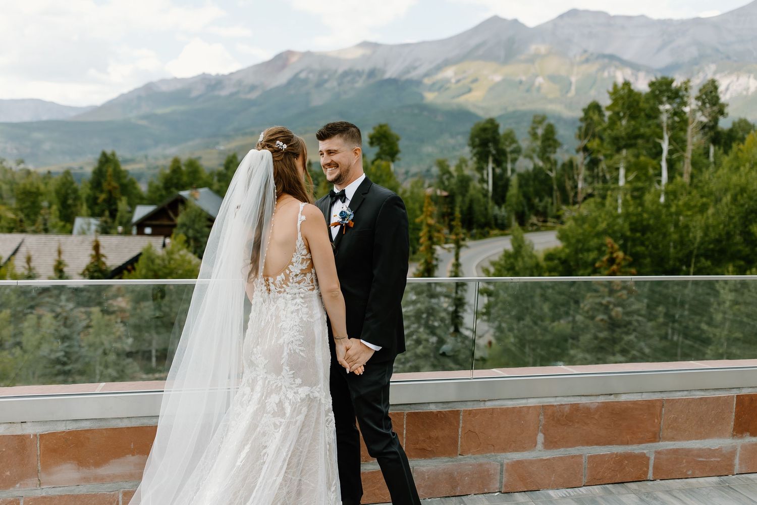 A wedding couple shares an intimate moment on a mountain terrace with dramatic peaks in the background.