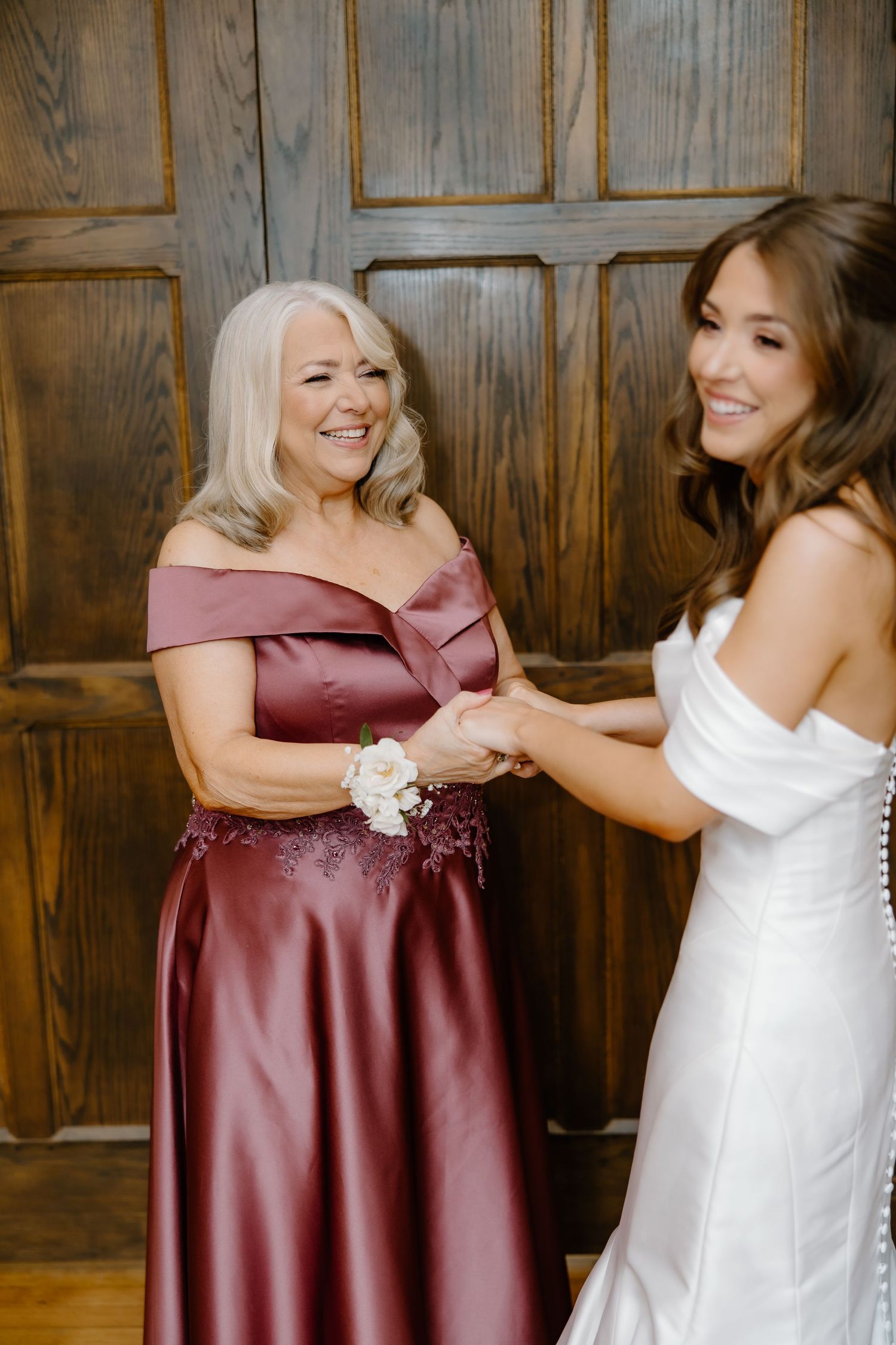Wedding party in burgundy dresses sharing joyful moments against wood paneled walls.