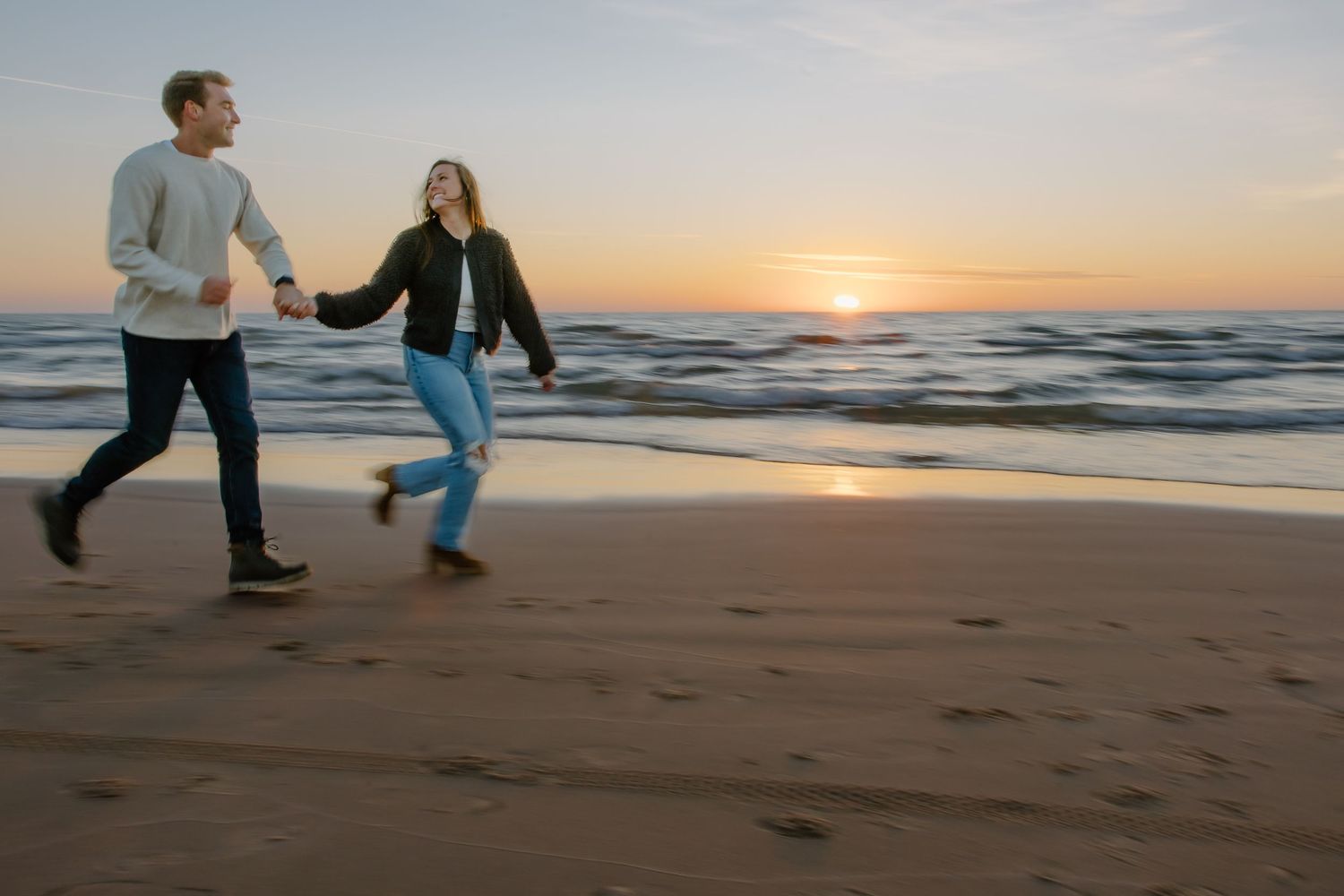 Couple holding hands and spinning in a dance on the beach during golden hour.