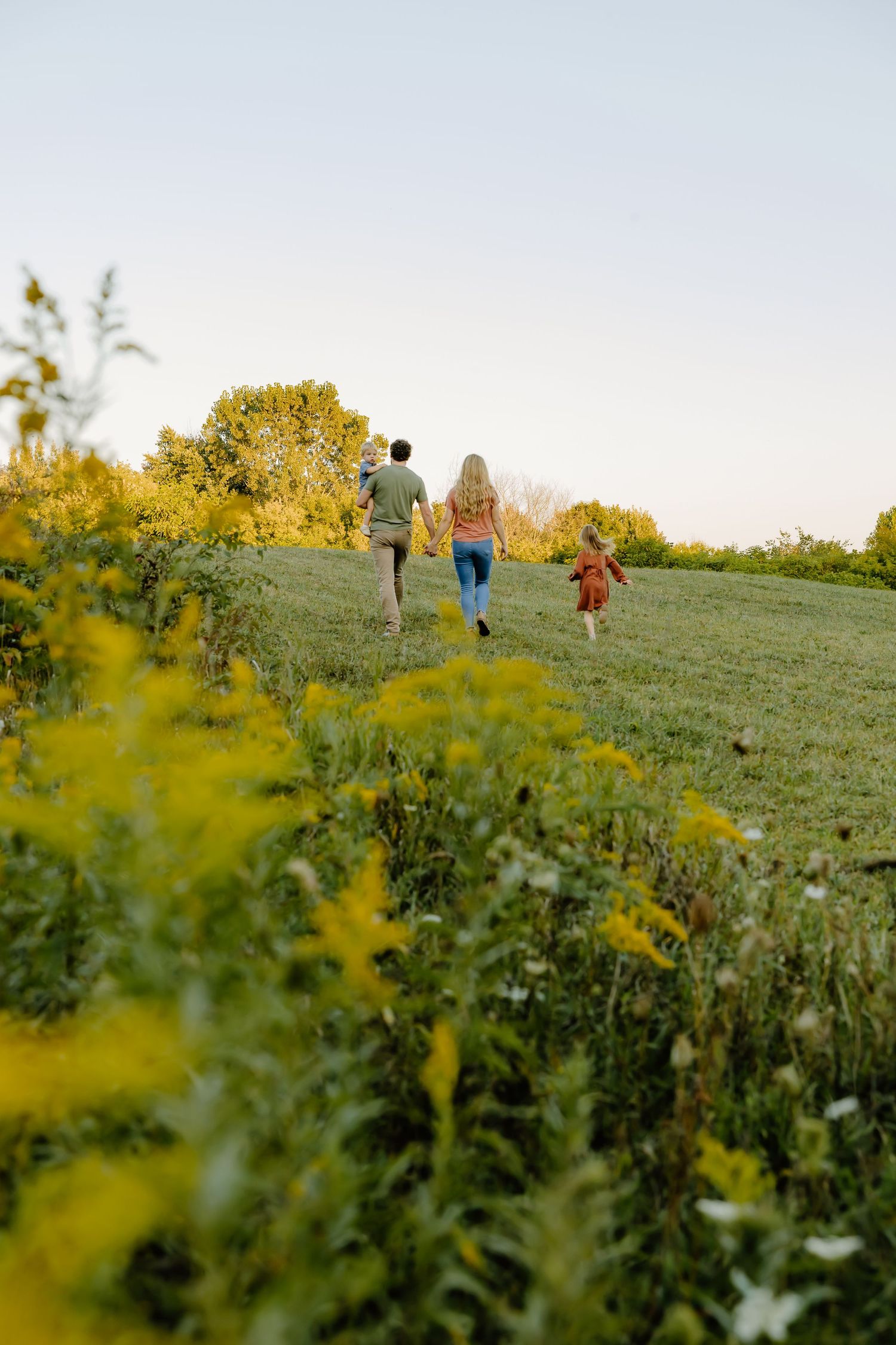 People walking through a meadow with yellow wildflowers during golden hour.