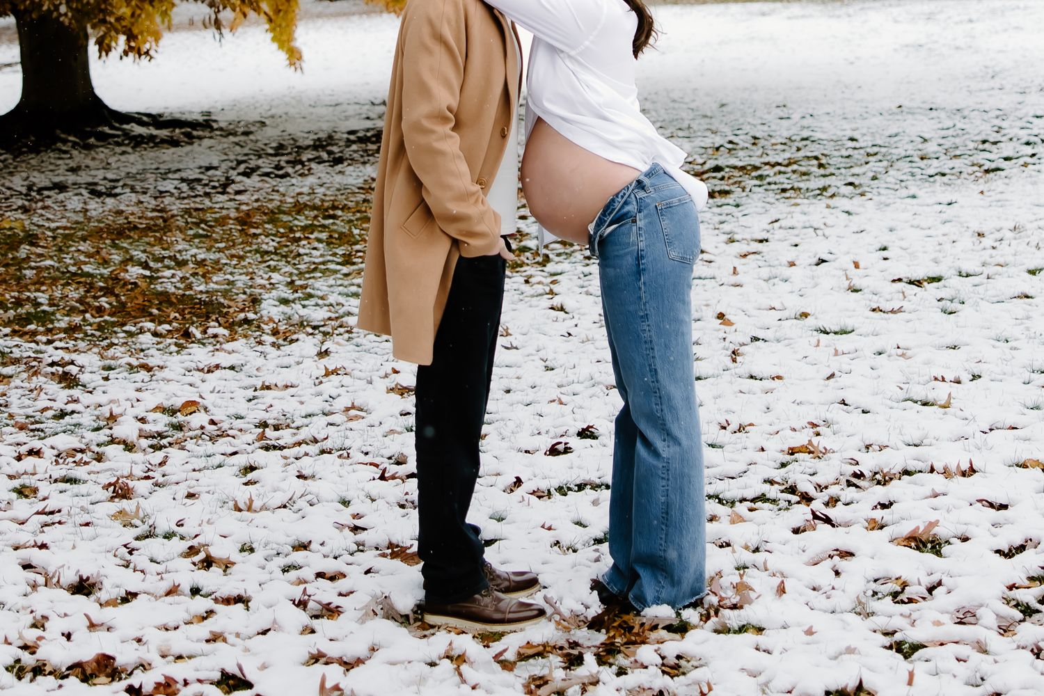 Close up of couple's legs standing together in snow, wearing jeans and boots.