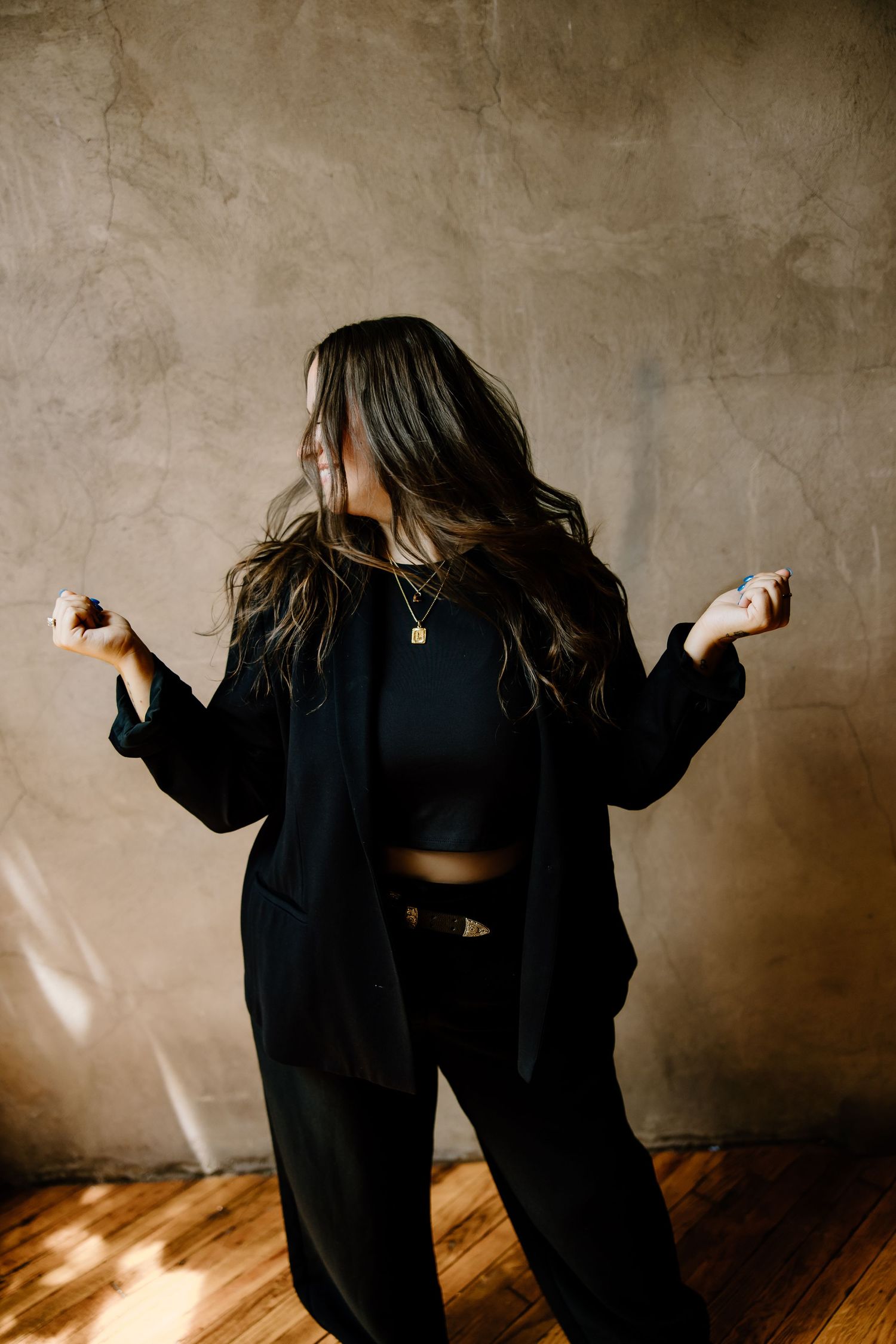 Two figures in black clothing dance together against a textured brown wall with dramatic lighting and wooden flooring.