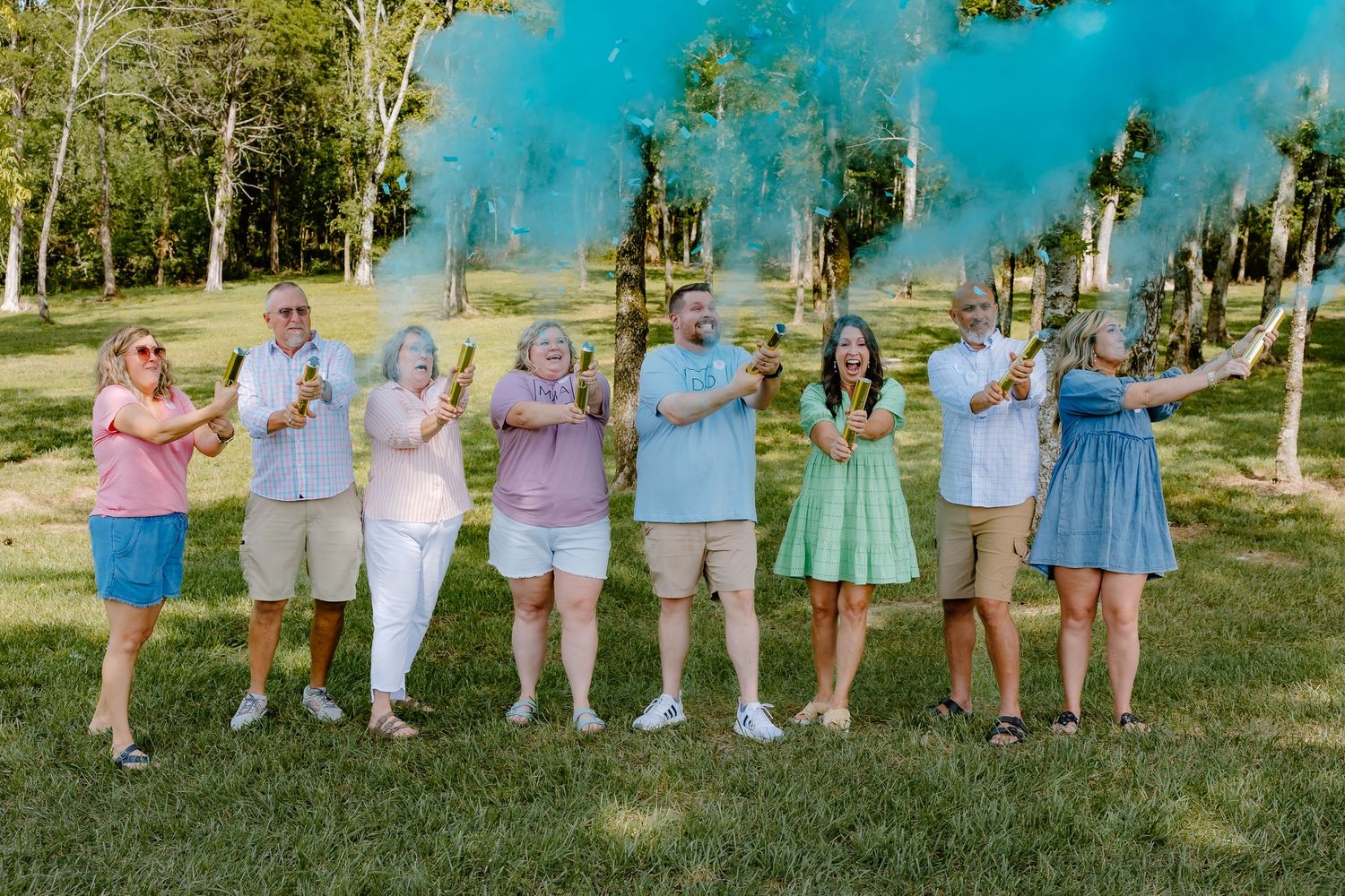Large group photo with blue smoke effect during outdoor gender reveal celebration.