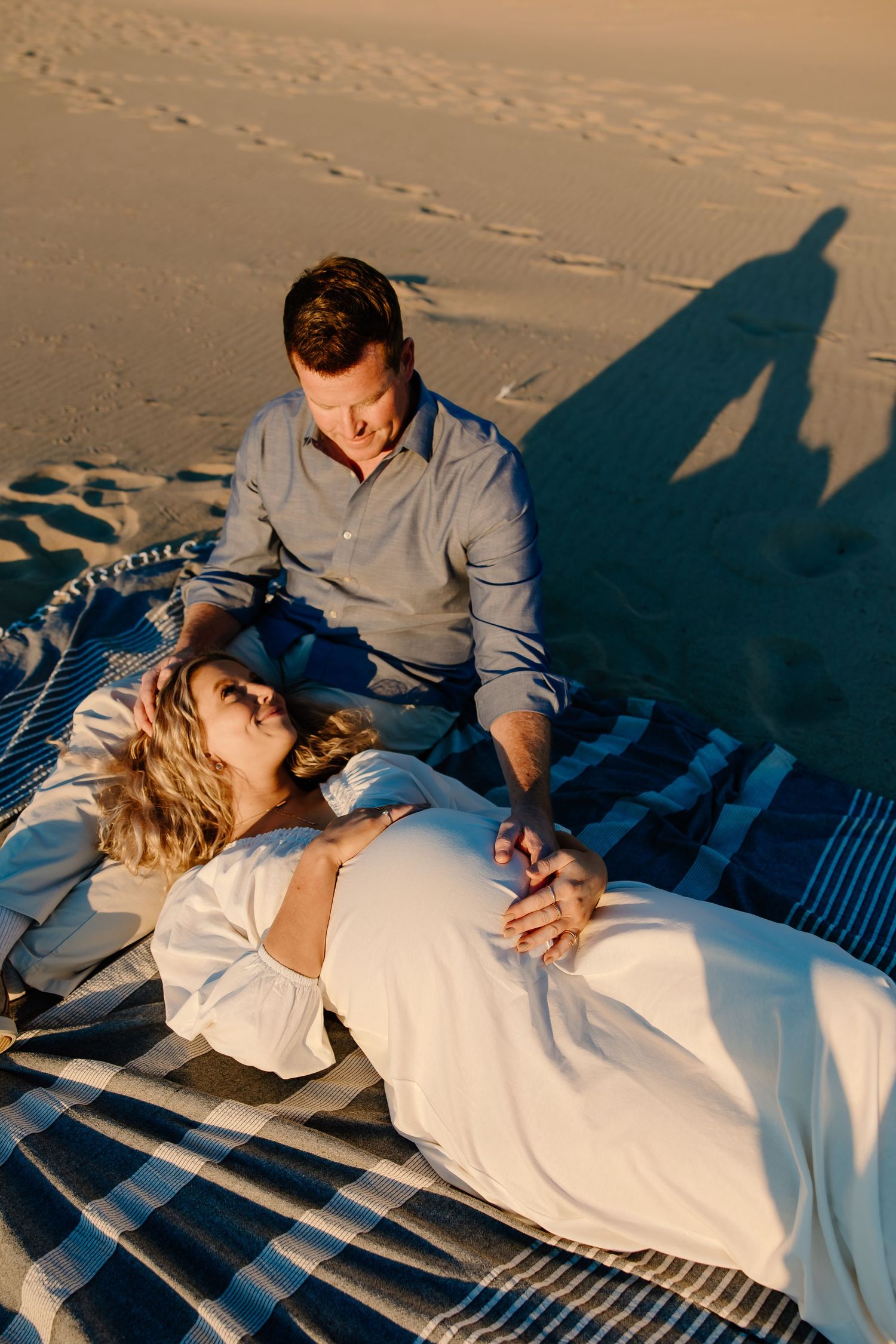 Romantic beach picnic scene with couple lounging on striped blanket at sunset.