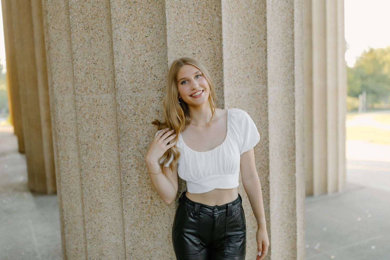 Casual fashion portrait of a person in a white crop top and black leather pants posing between stone columns.
