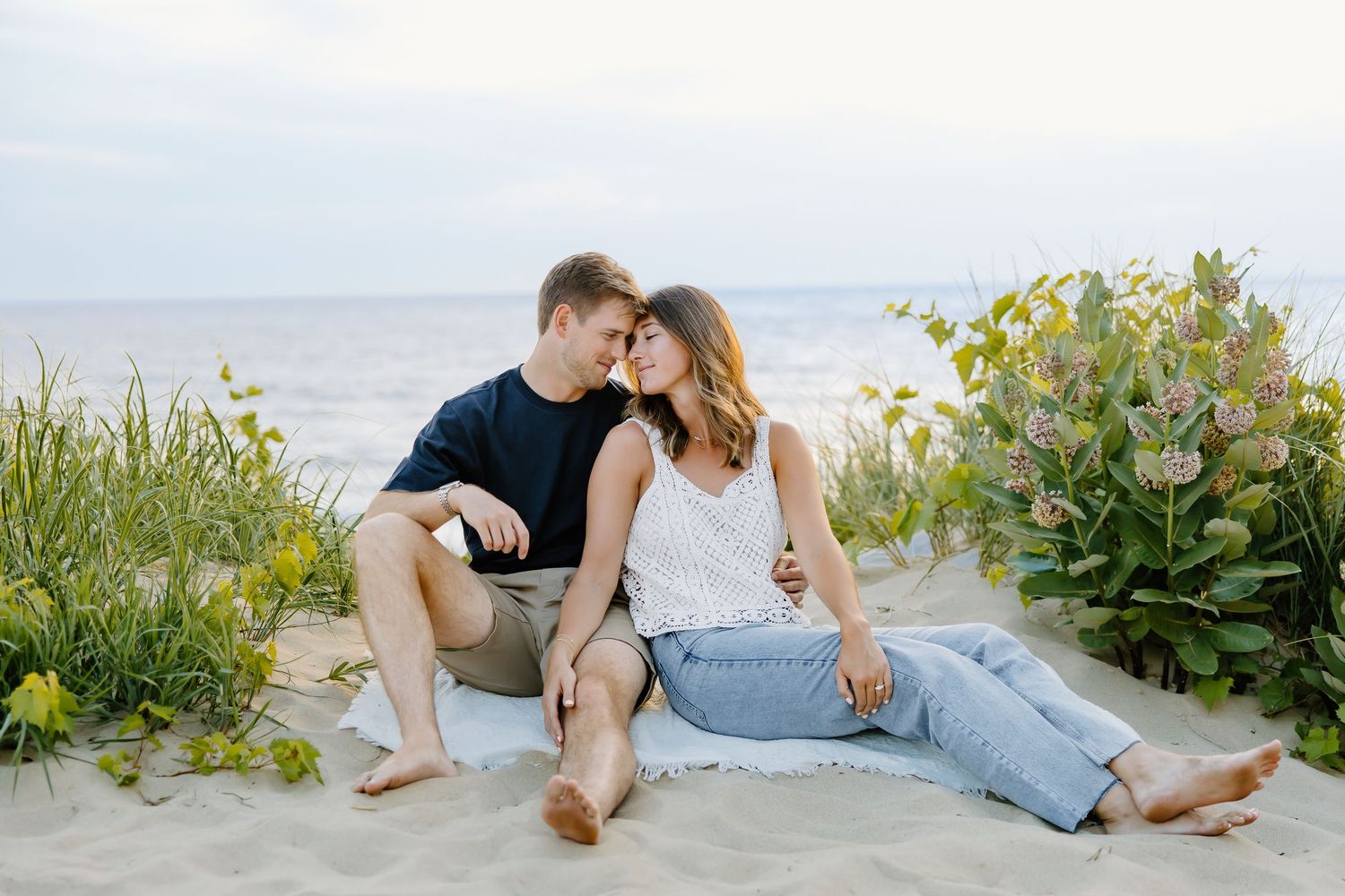 Couple relaxing together on a sandy beach with coastal plants and ocean views.