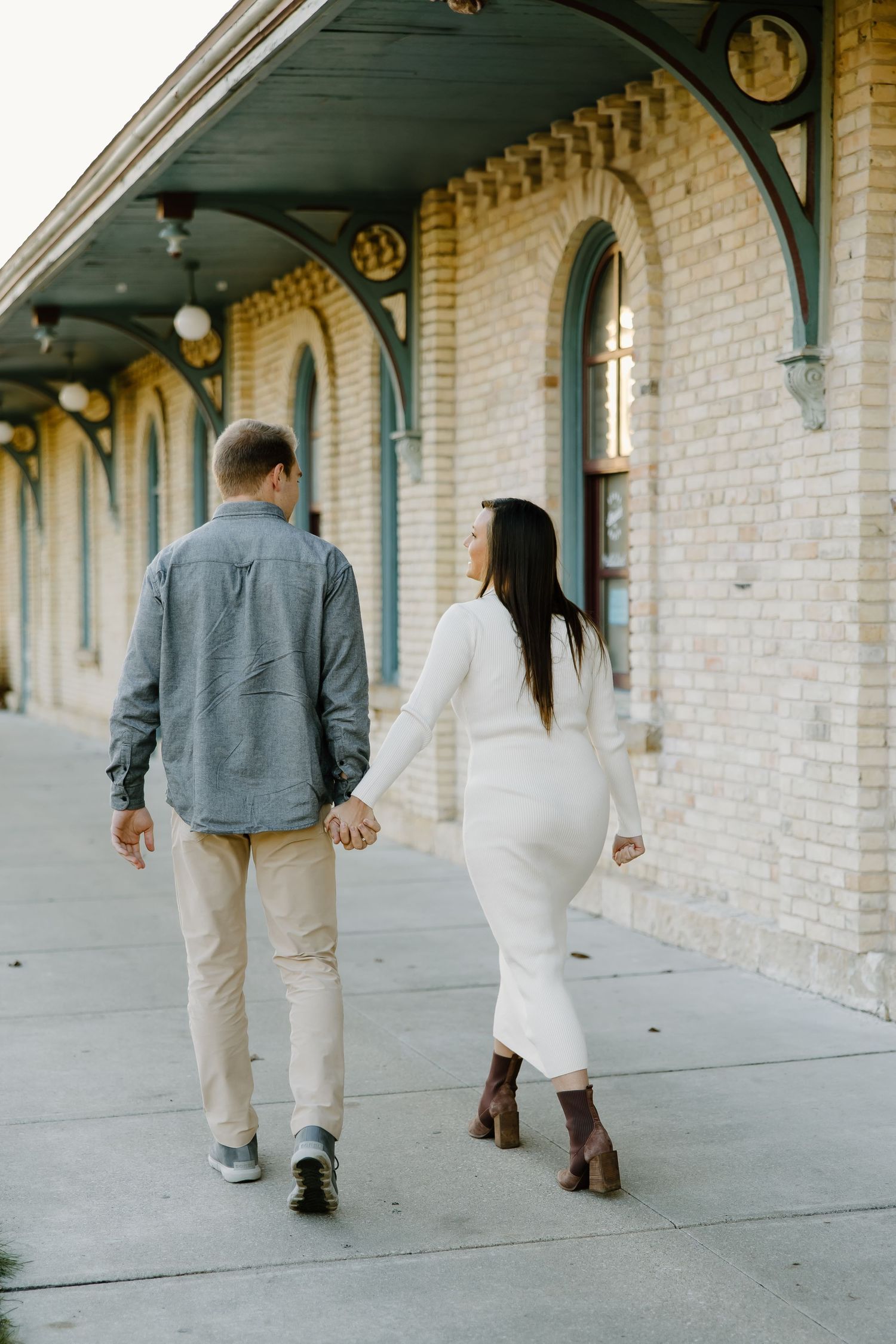 People walking along a covered brick walkway with architectural details.