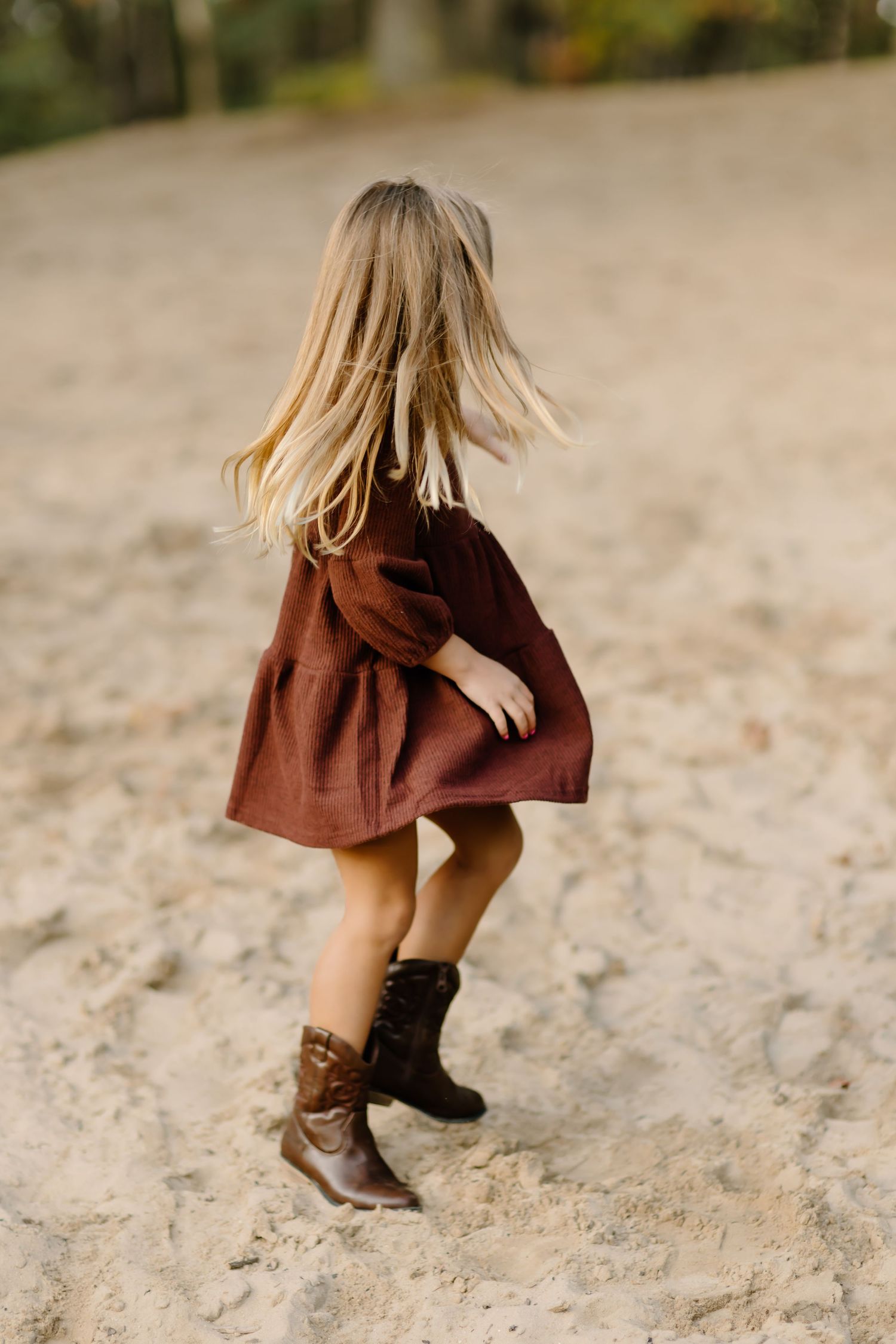 Close-up of brown boots and burgundy dress on sandy ground during autumn photoshoot.