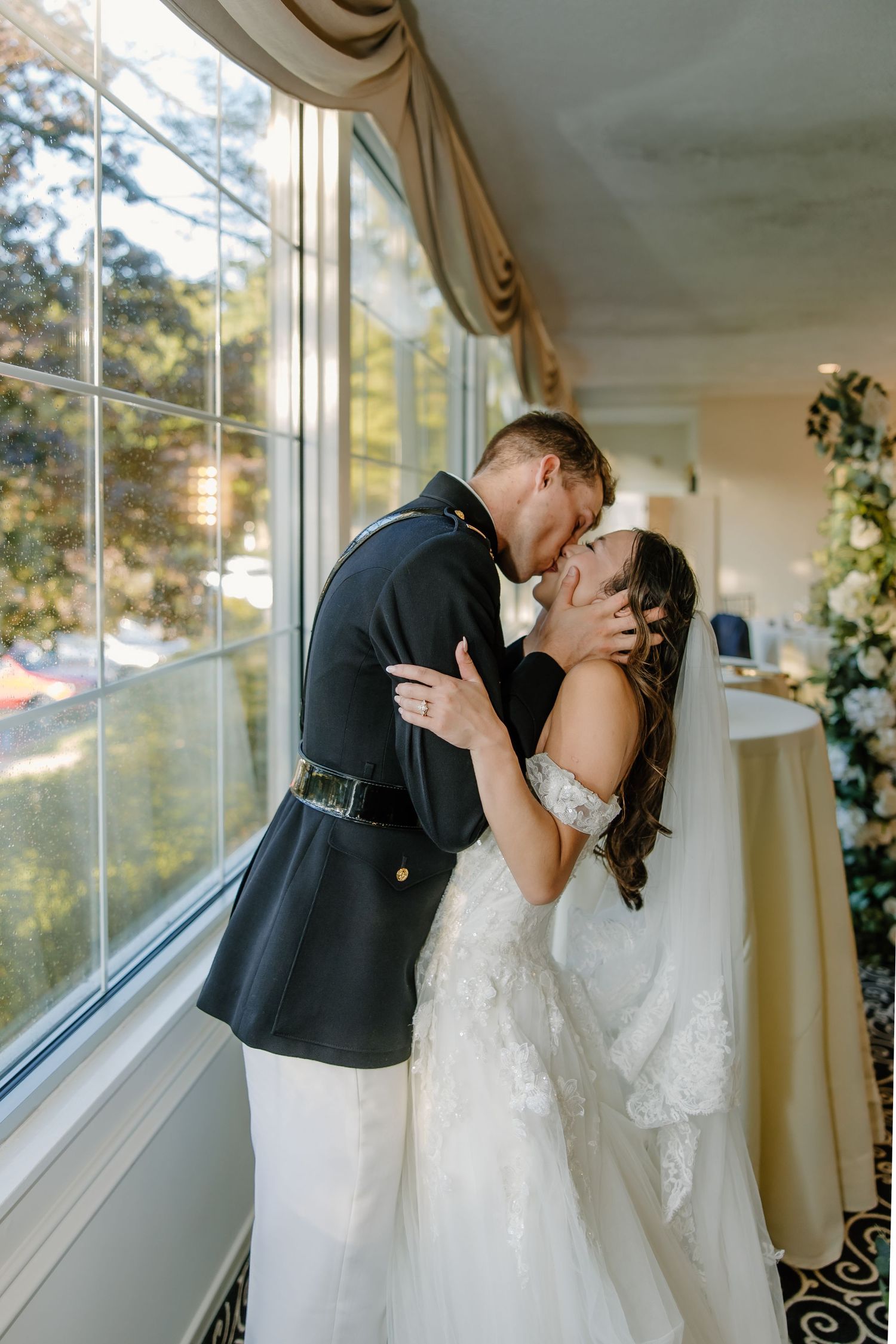 Romantic wedding couple sharing intimate kisses by sunlit windows in an elegant indoor setting.
