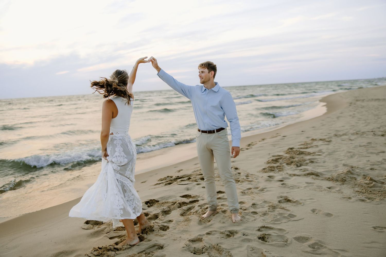 Couple dancing on beach sand at sunset with white dress flowing.