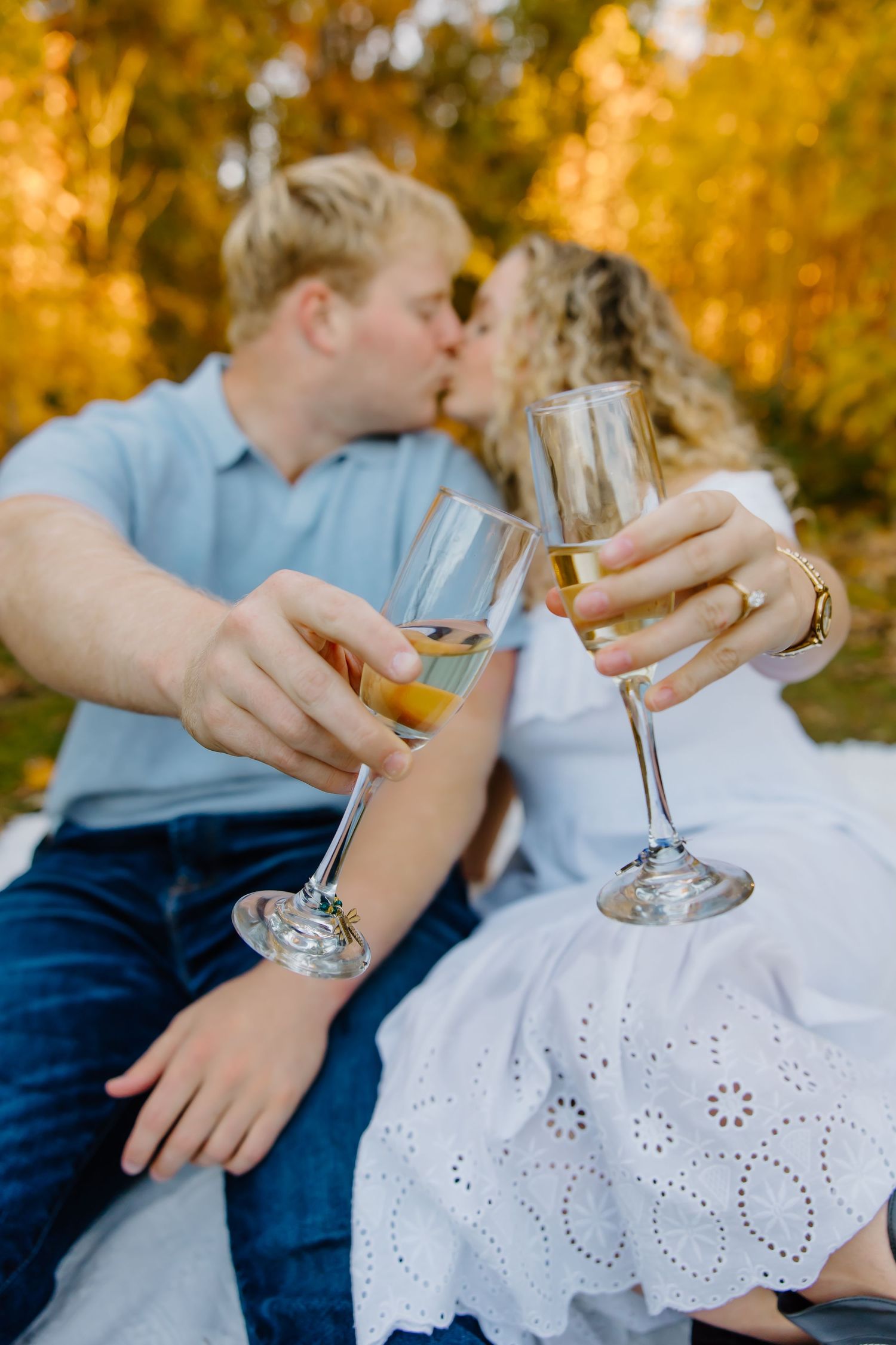Close-up of hands holding champagne glasses against autumn foliage background.