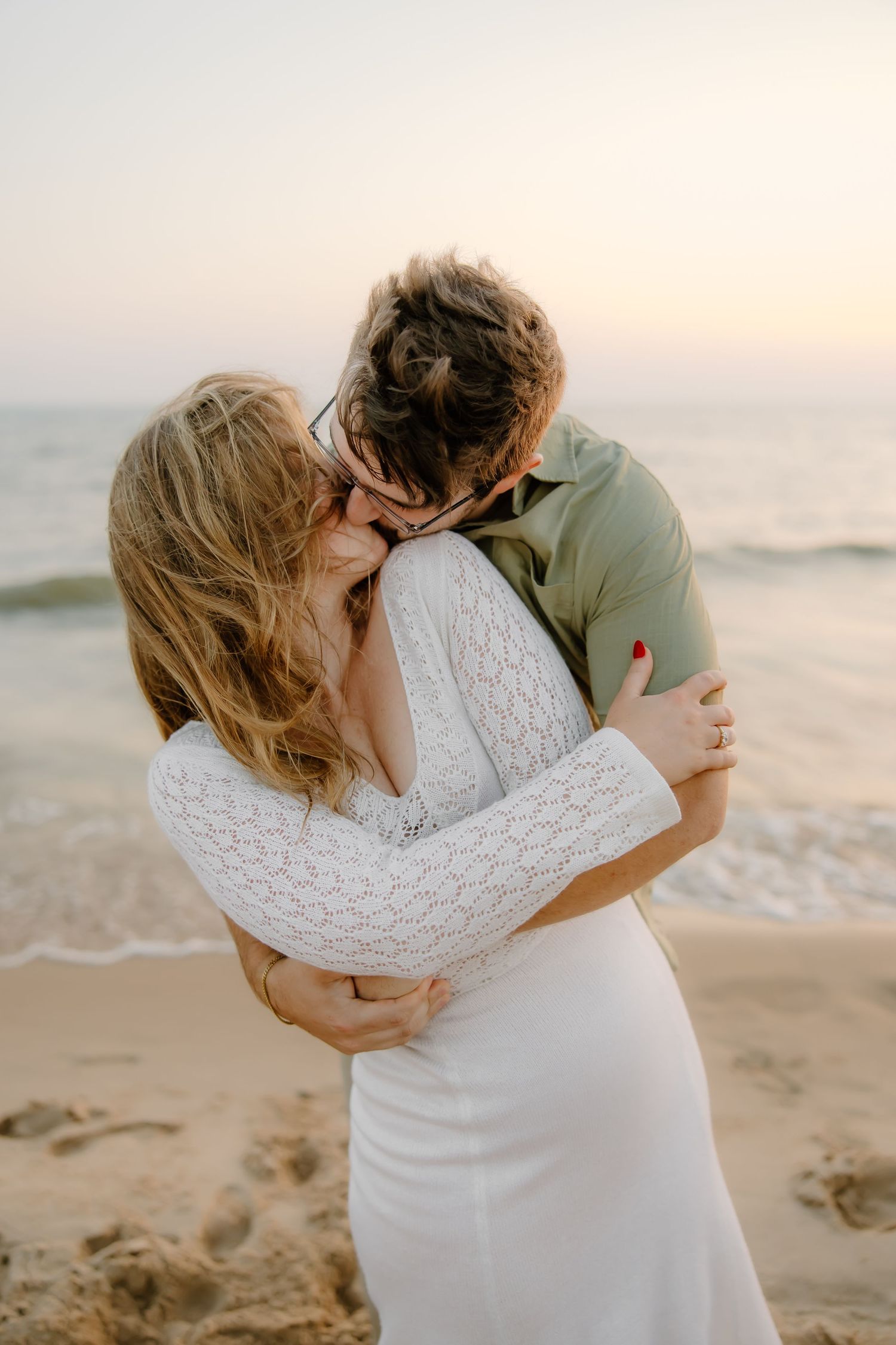An intimate beach photoshoot featuring a couple embracing in white and sage green outfits.