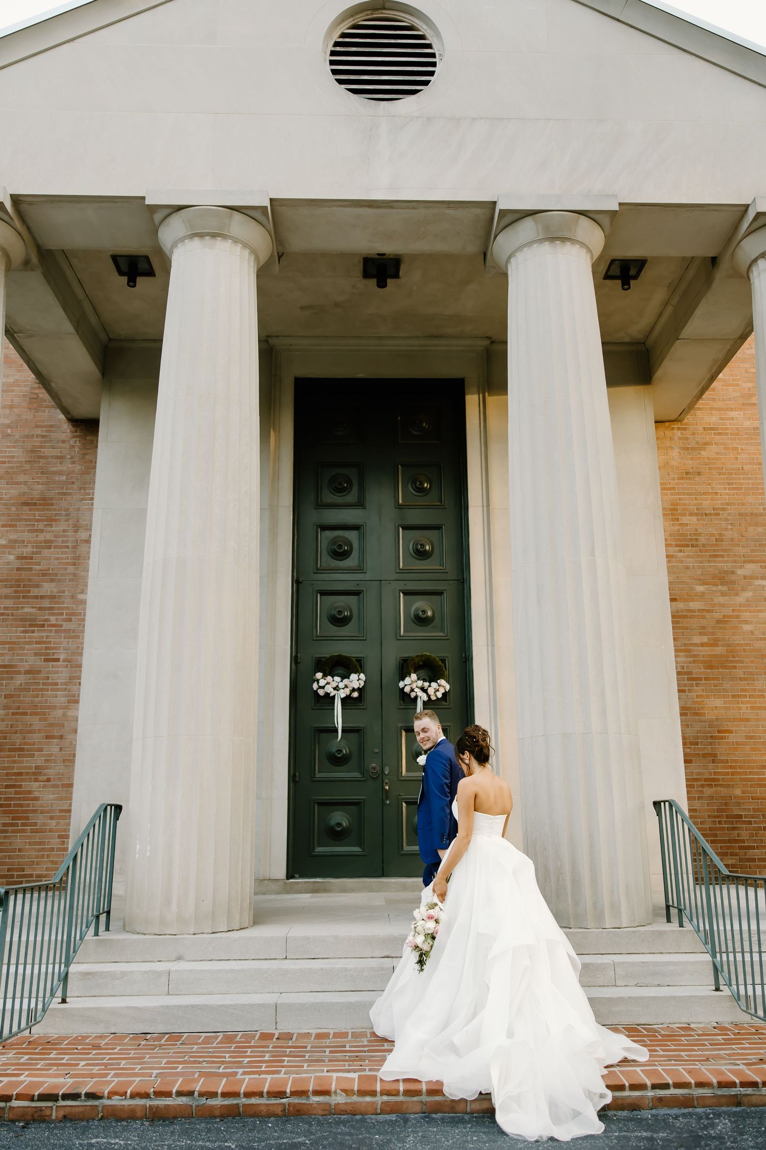 Wedding portraits on steps of brick building with white columns.