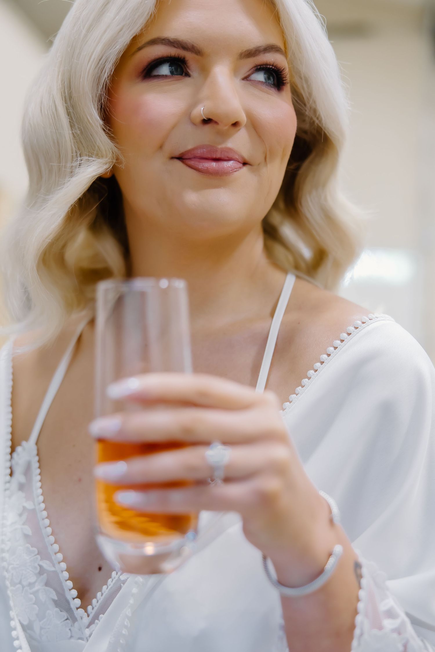 Bride in white robe enjoying a drink during wedding preparations.