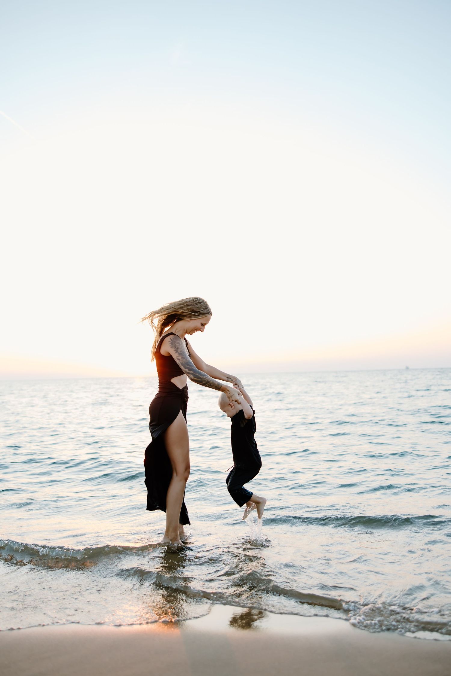 People playing in the shallow ocean water during a serene sunset.