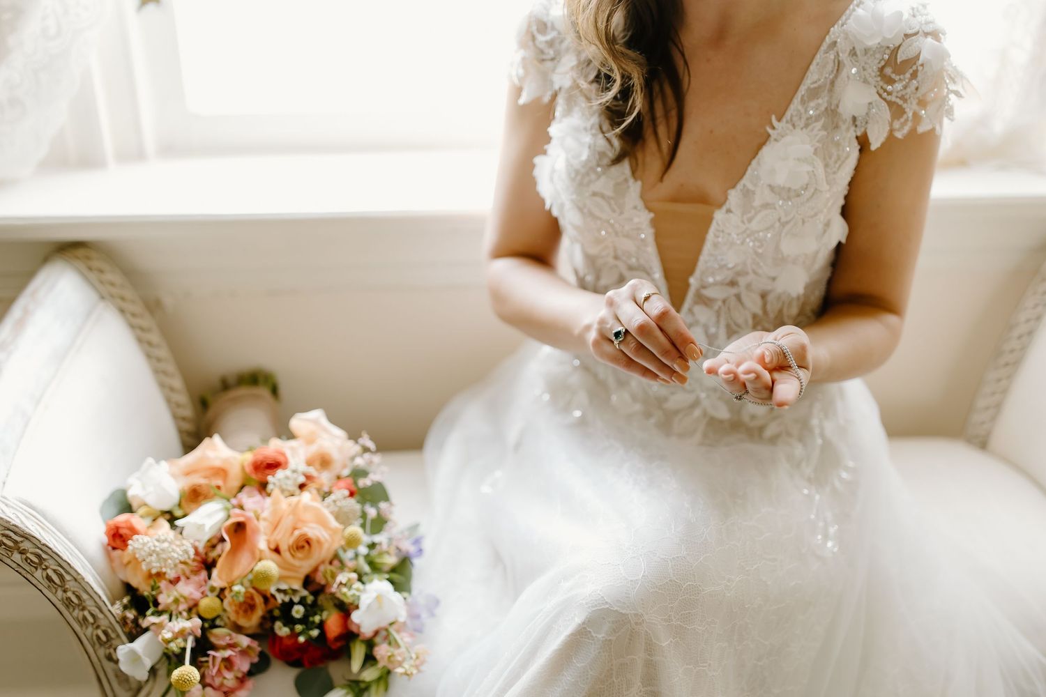 Close-up details of a white lace wedding dress and peach-colored floral bouquet.